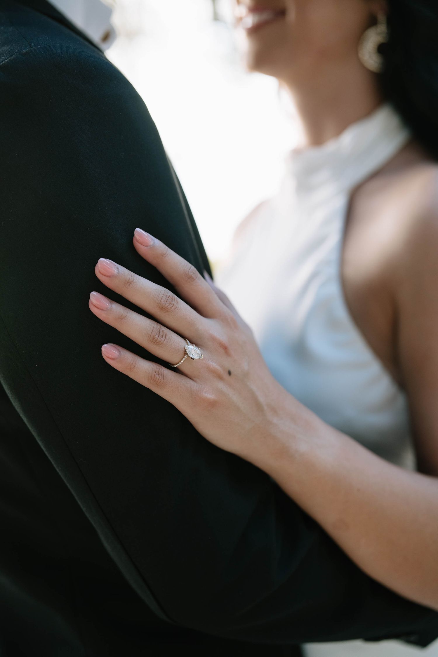 Close-up of an engagement ring on a hand against a dark background.