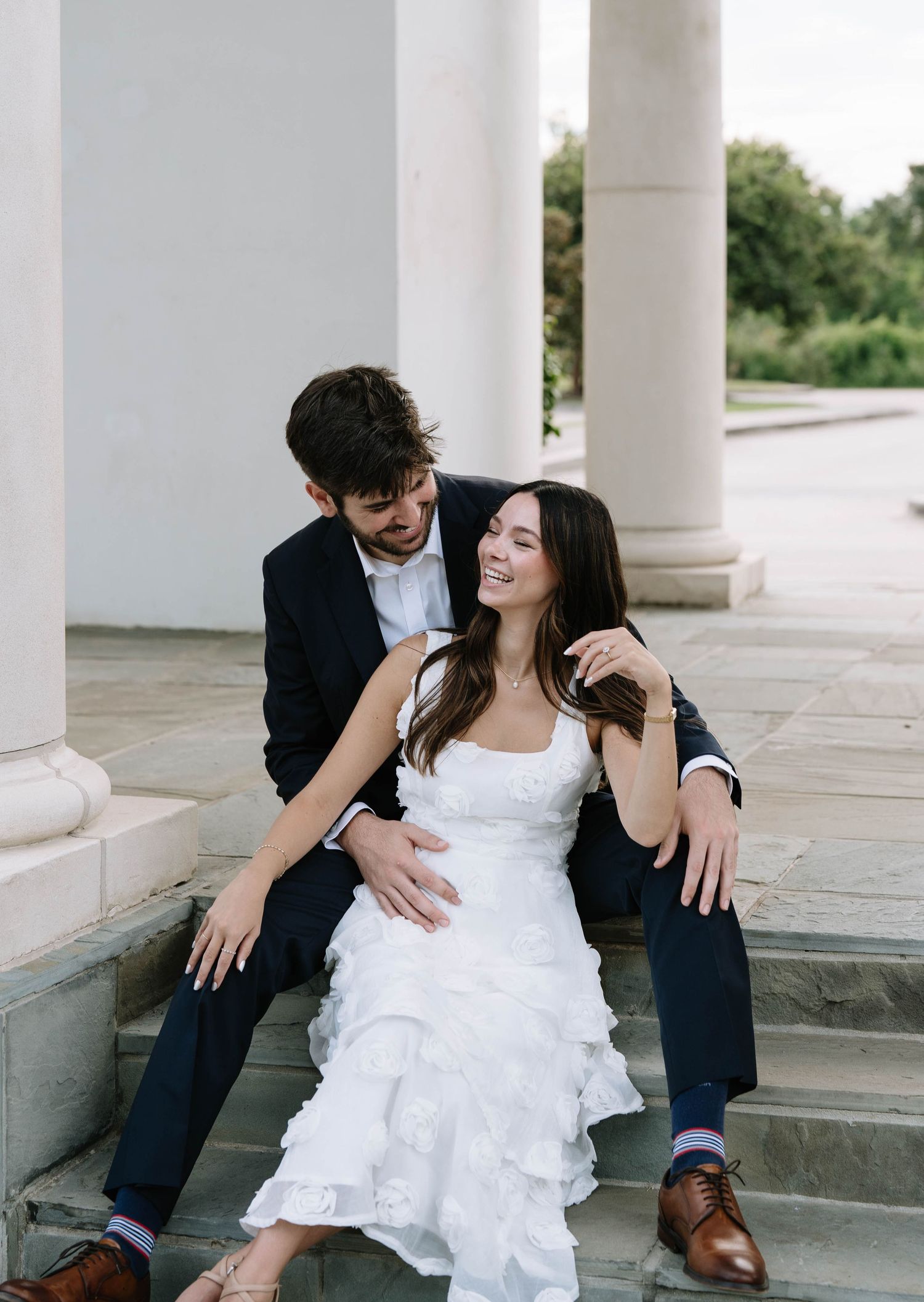 Couple shares intimate moment on marble steps surrounded by white columns.