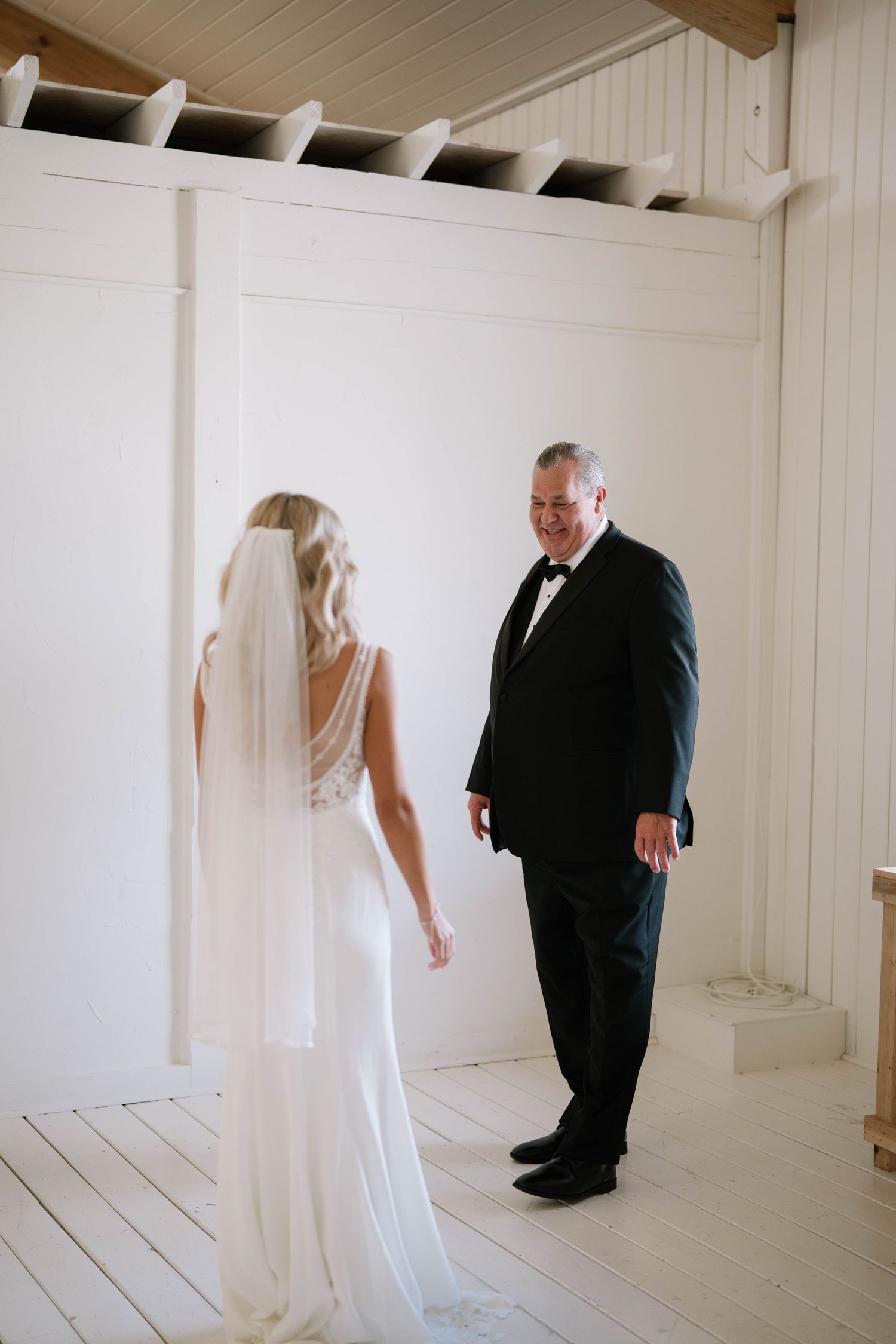 Wedding couple in white dress and black suit in minimalist white room with wooden ceiling beams.
