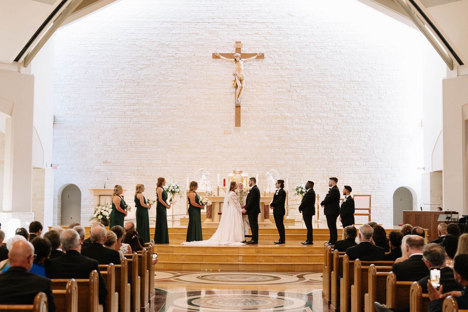 Interior view of a church wedding ceremony with guests seated in wooden pews under vaulted ceiling.