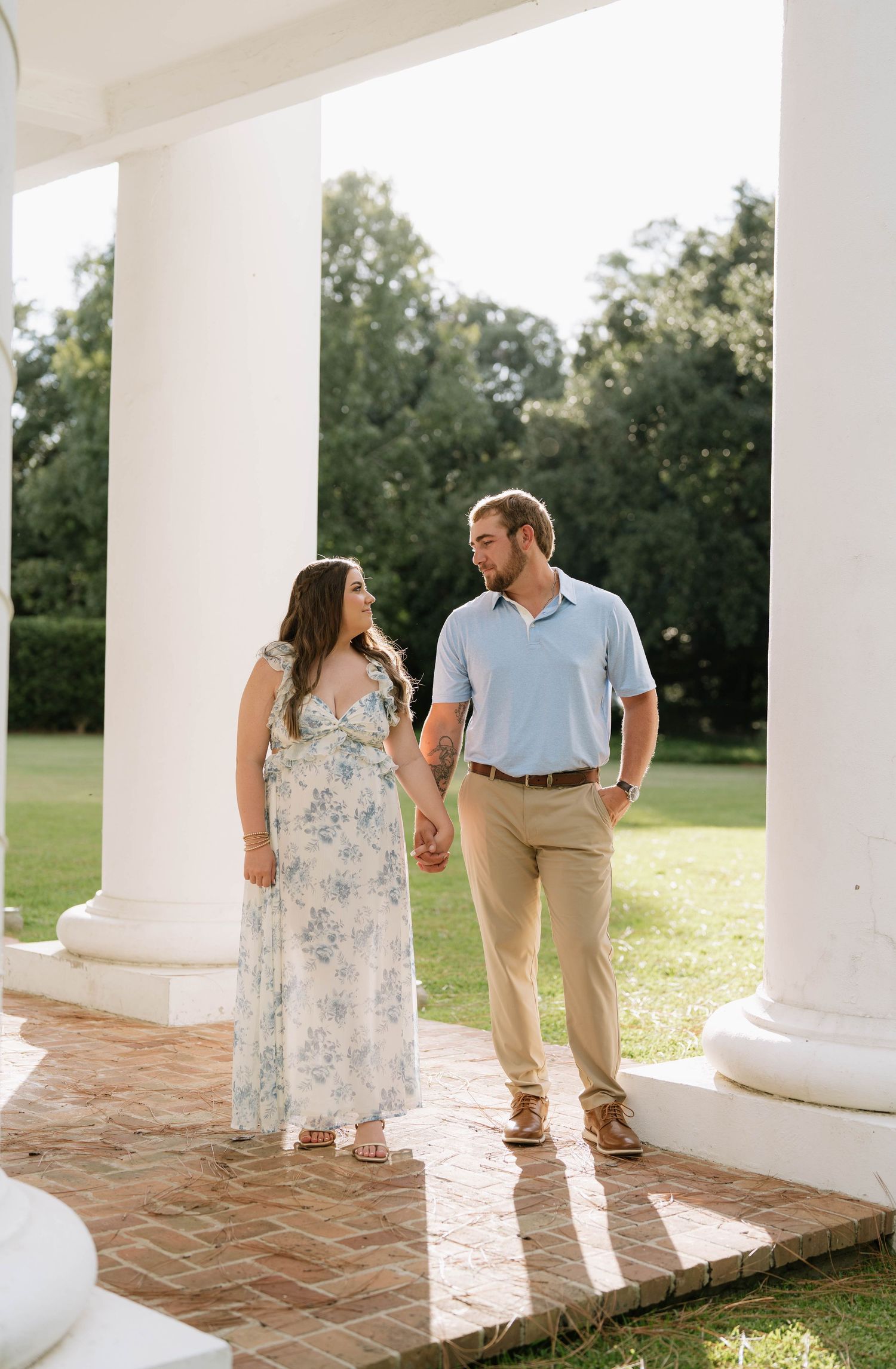 Romantic couple strolling under white columns in summer attire during golden hour.