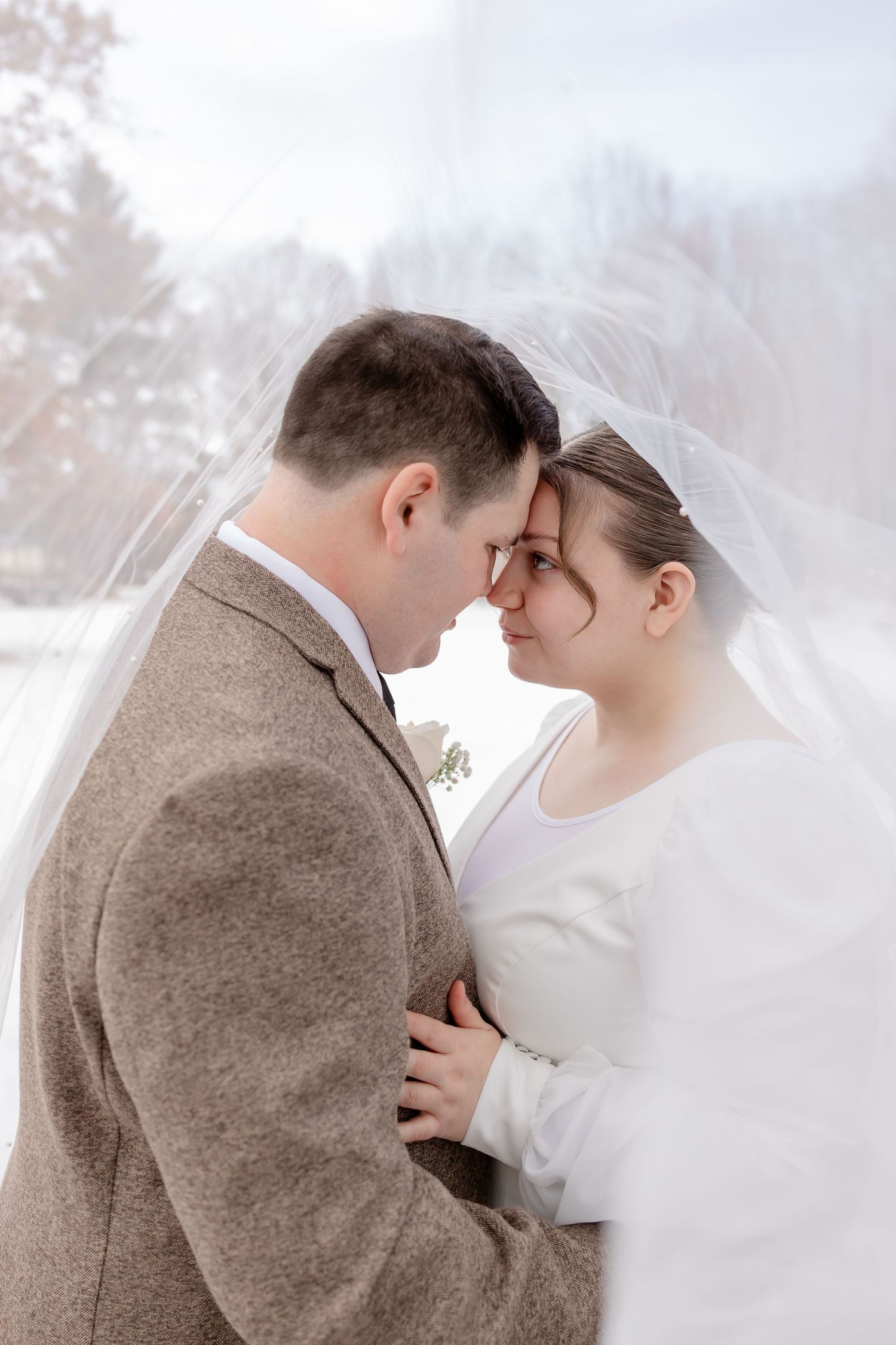 Intimate winter wedding portrait showing tender moment between couple in brown and white attire.