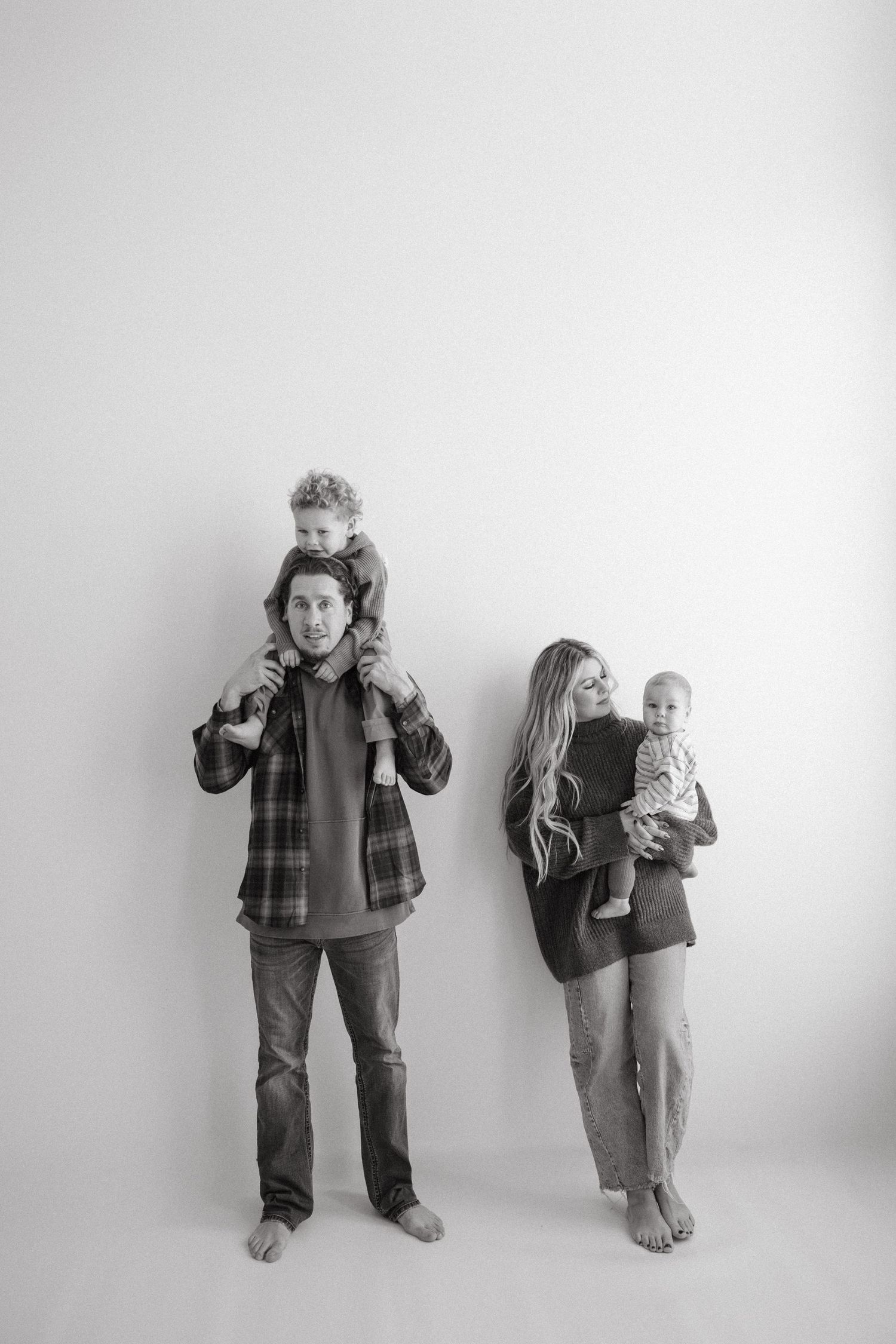 Black and white studio portrait of a family with two young children against a plain wall background.