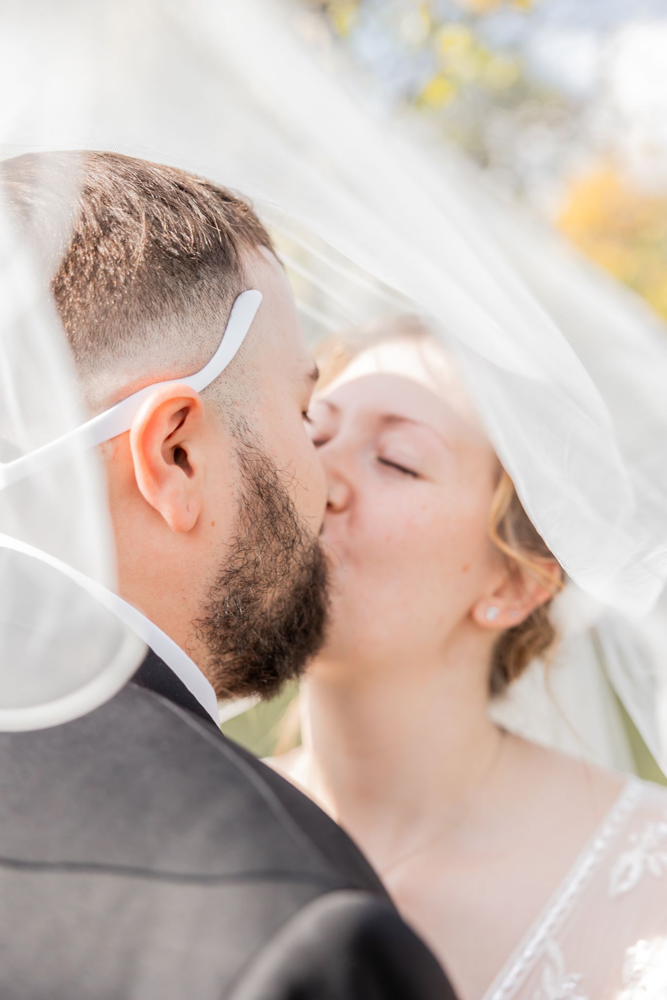 Romantic wedding photo of couple sharing a kiss under flowing white veil.