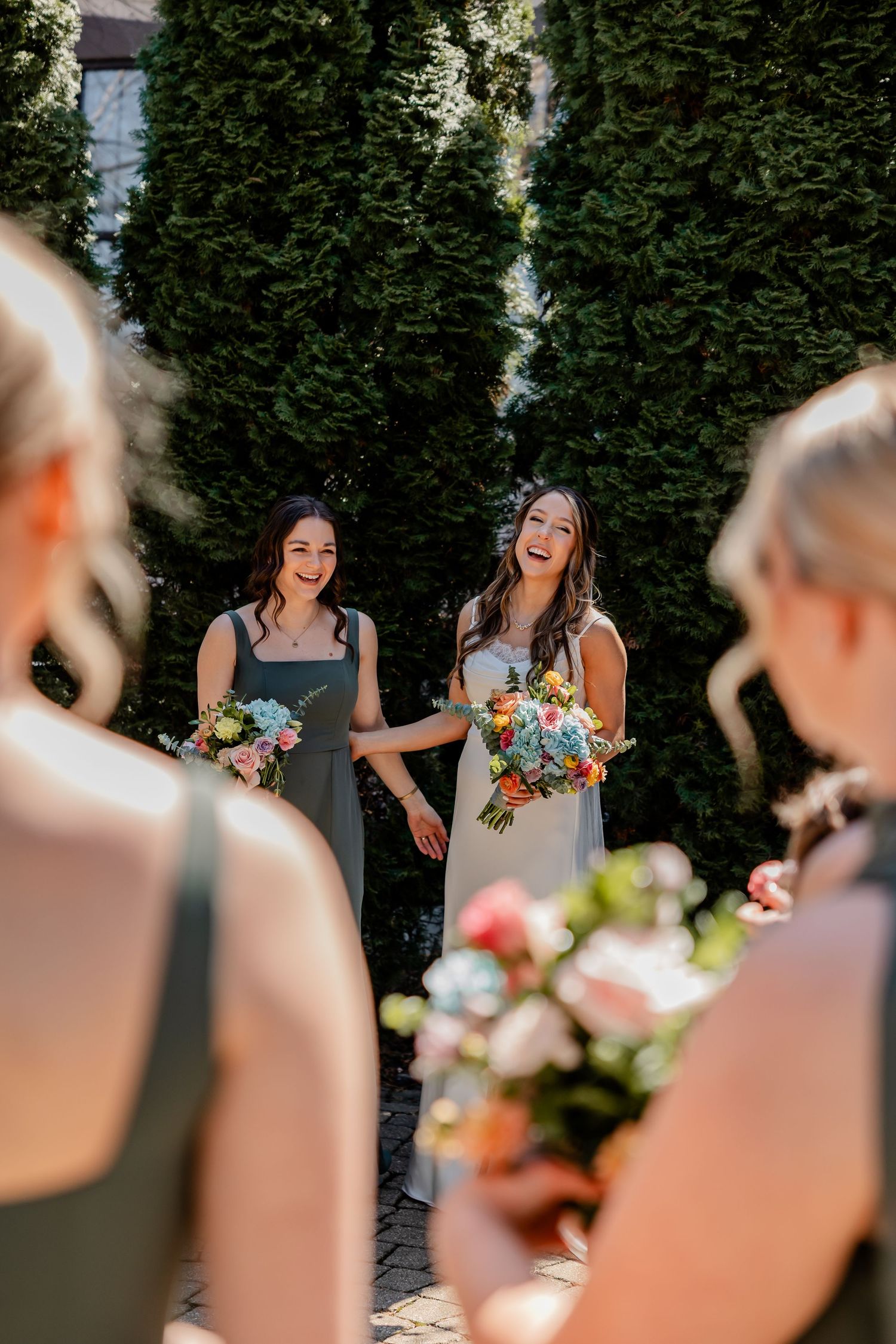 Bridesmaids with colorful bouquets share joyful laughter during outdoor wedding photos.