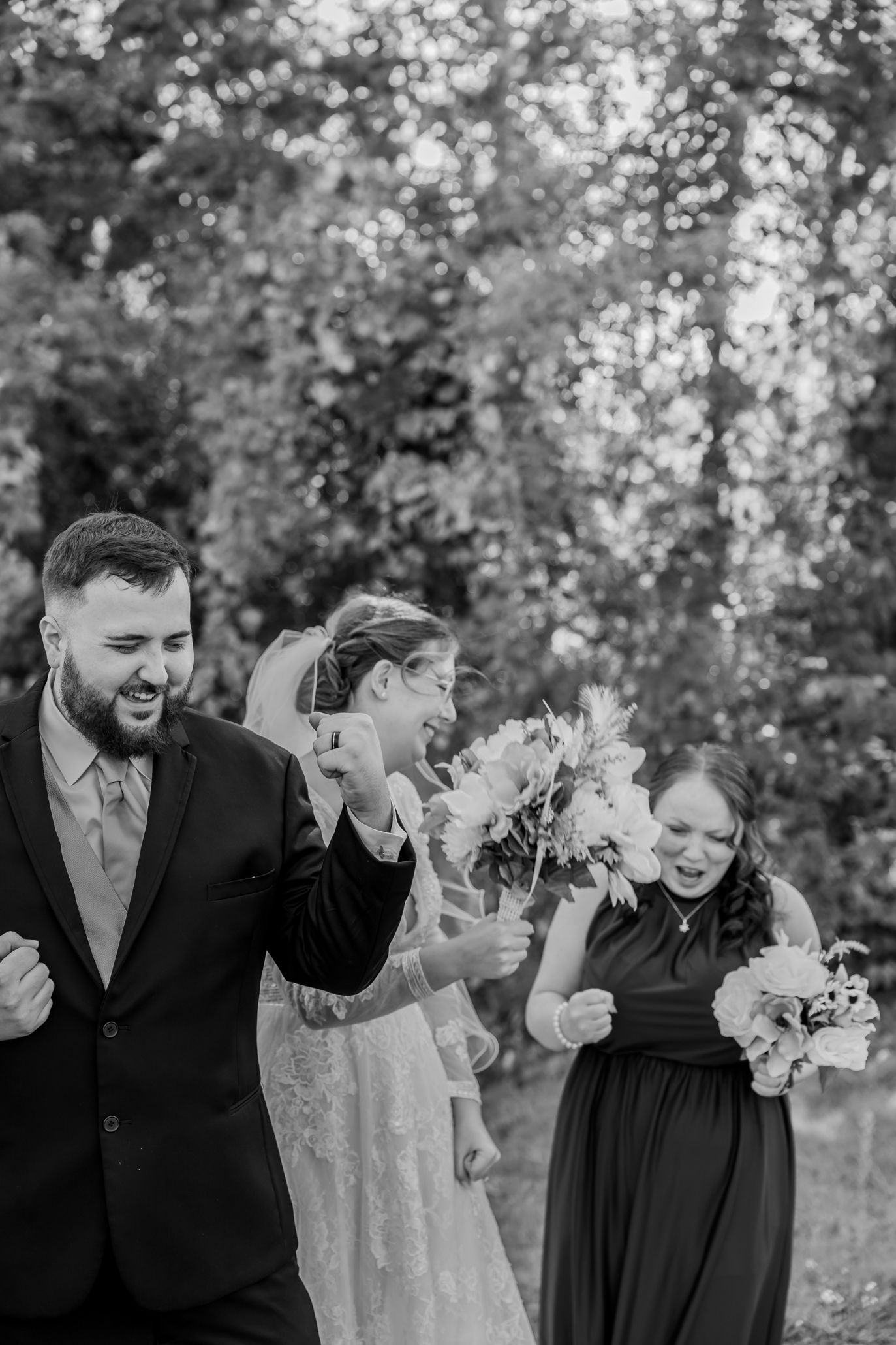 Wedding party members laugh together during outdoor black and white photo session.