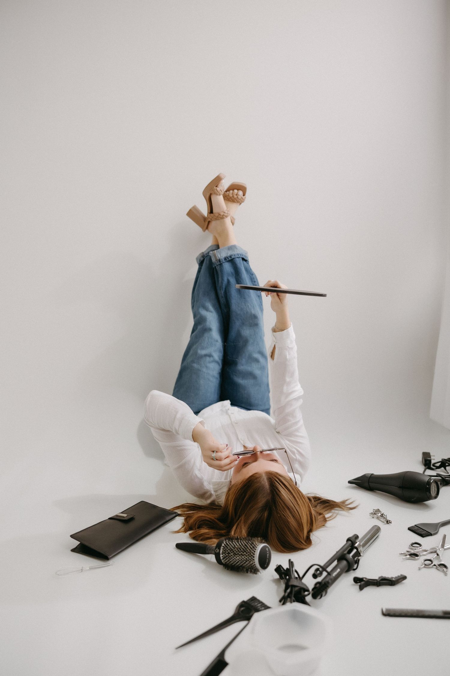 Person lying on white floor surrounded by scattered papers and office supplies in minimalist setting.