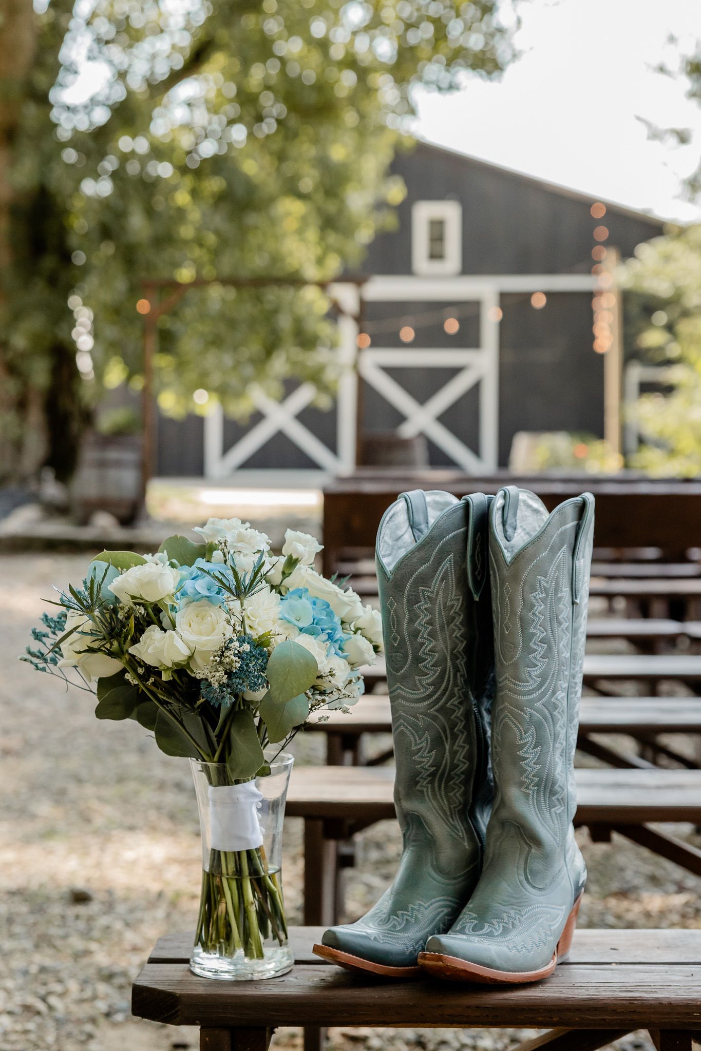 Turquoise cowboy boots paired with white floral bouquets arranged in mason jars on wooden benches at an outdoor venue.