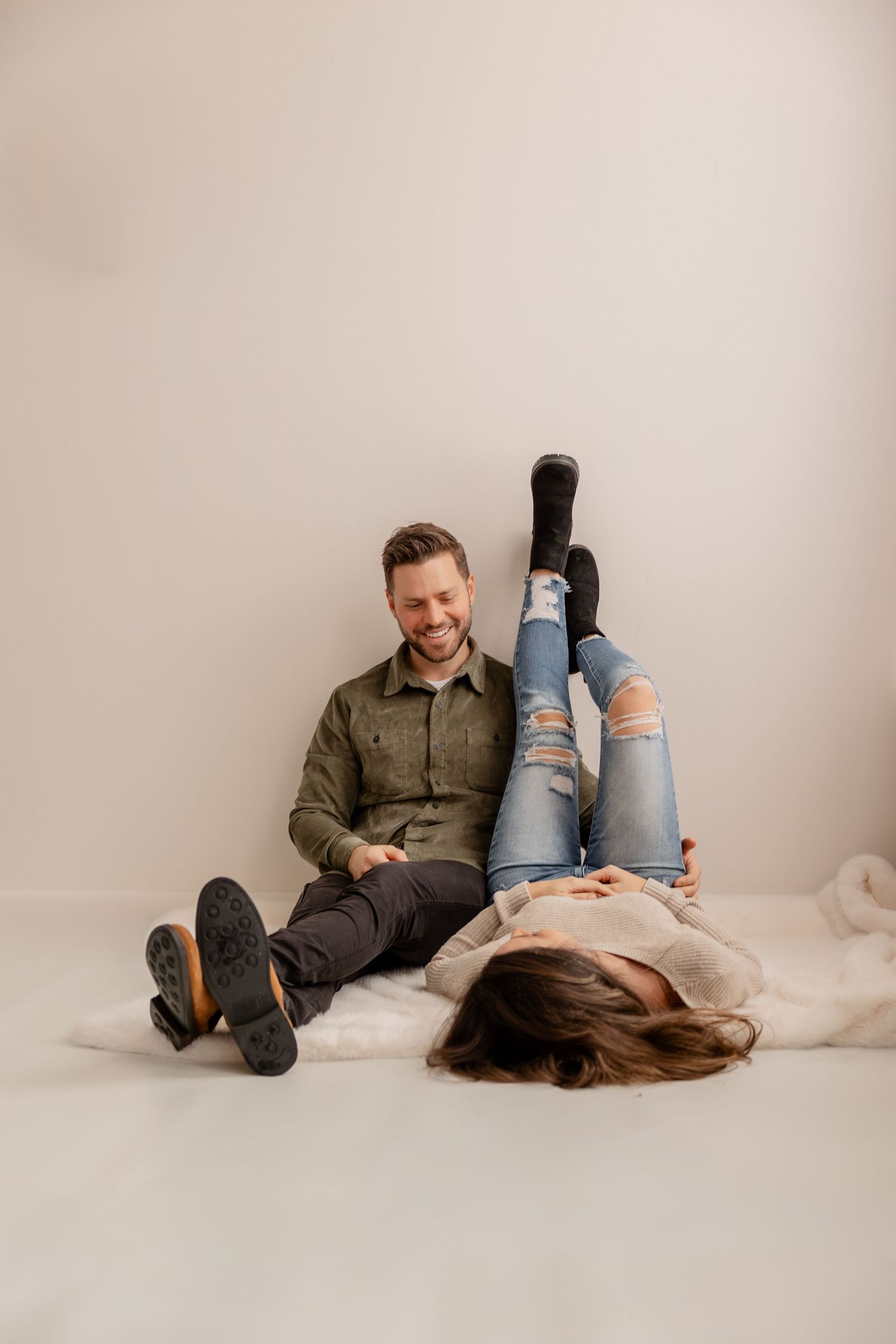 Two people relaxing and laughing together on a white floor, wearing casual clothing and distressed jeans.