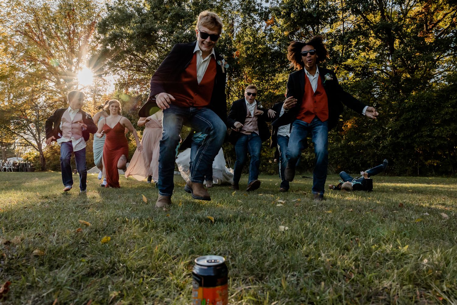 Wedding guests gathered on a grassy hill during golden hour with sunburst through trees.
