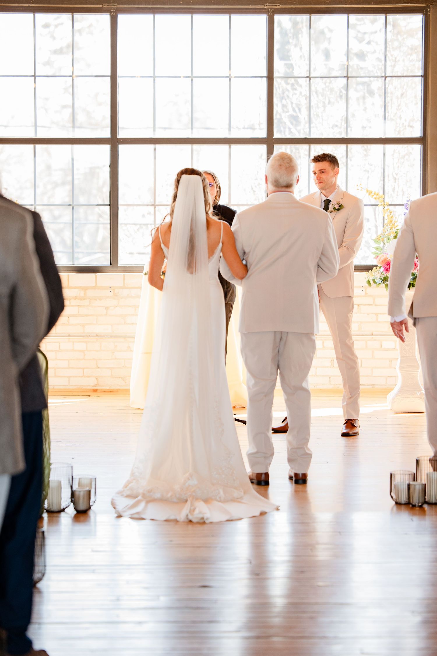 Wedding party silhouettes against large windows in an elegant indoor venue. Baker Loft