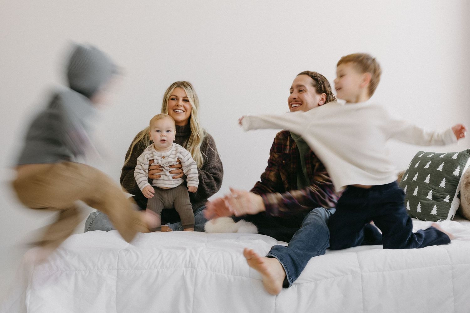 A sequence of black and white photos showing a family lounging and playing together on a bed.