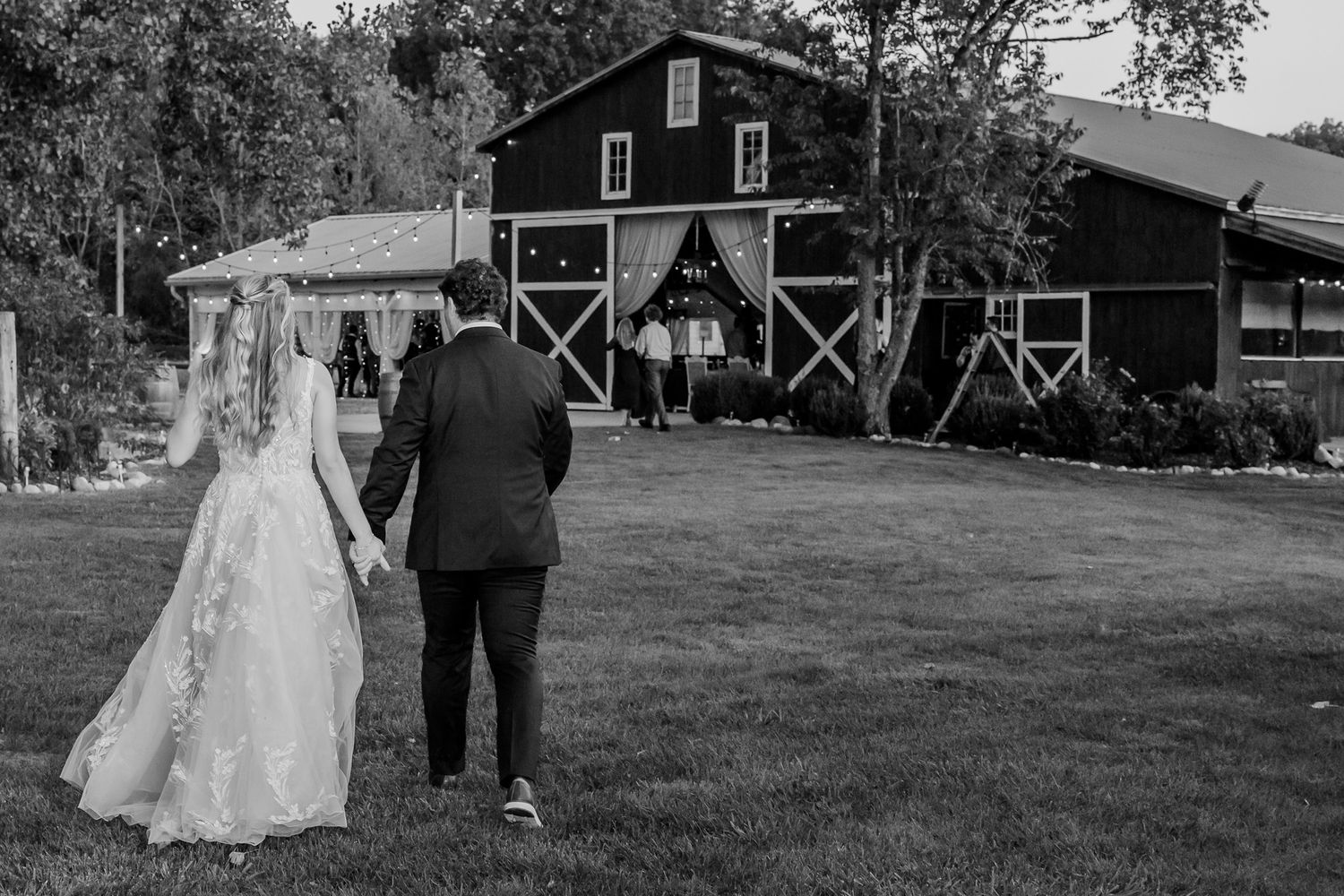 A black and white photo series captures an outdoor wedding ceremony with rustic barn and pastoral scenery.