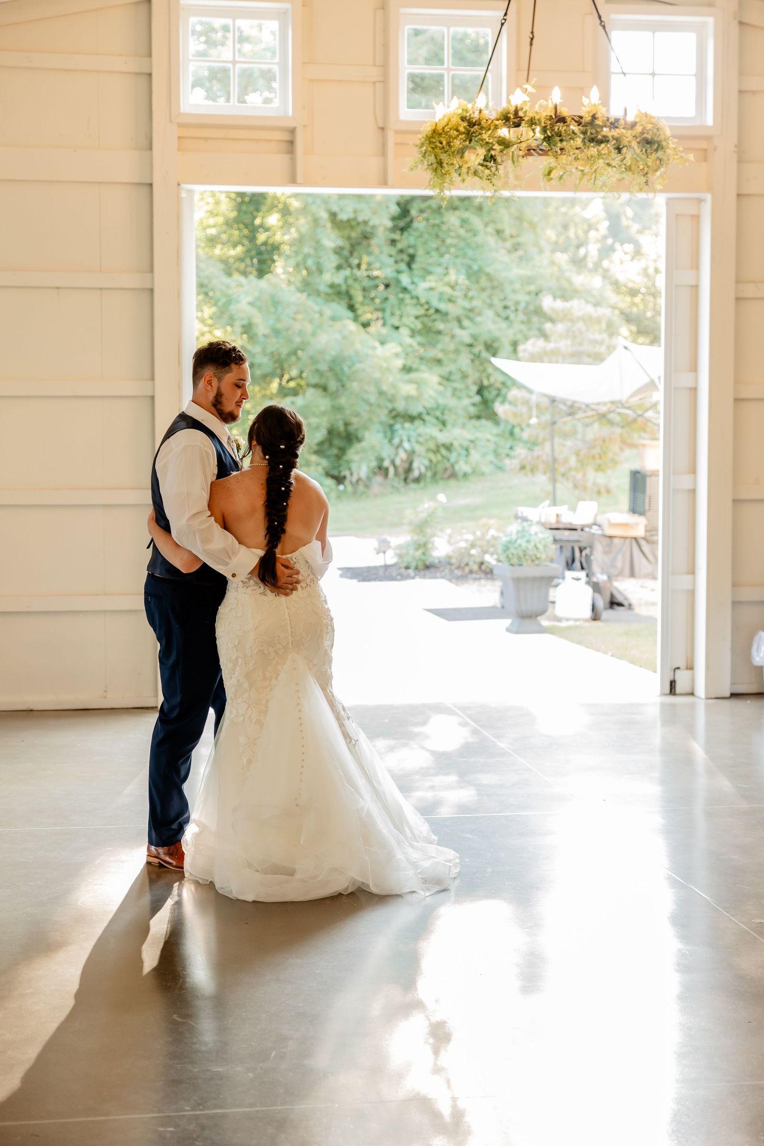 A couple shares an intimate dance moment in a bright white indoor venue with wooden beams and natural light.