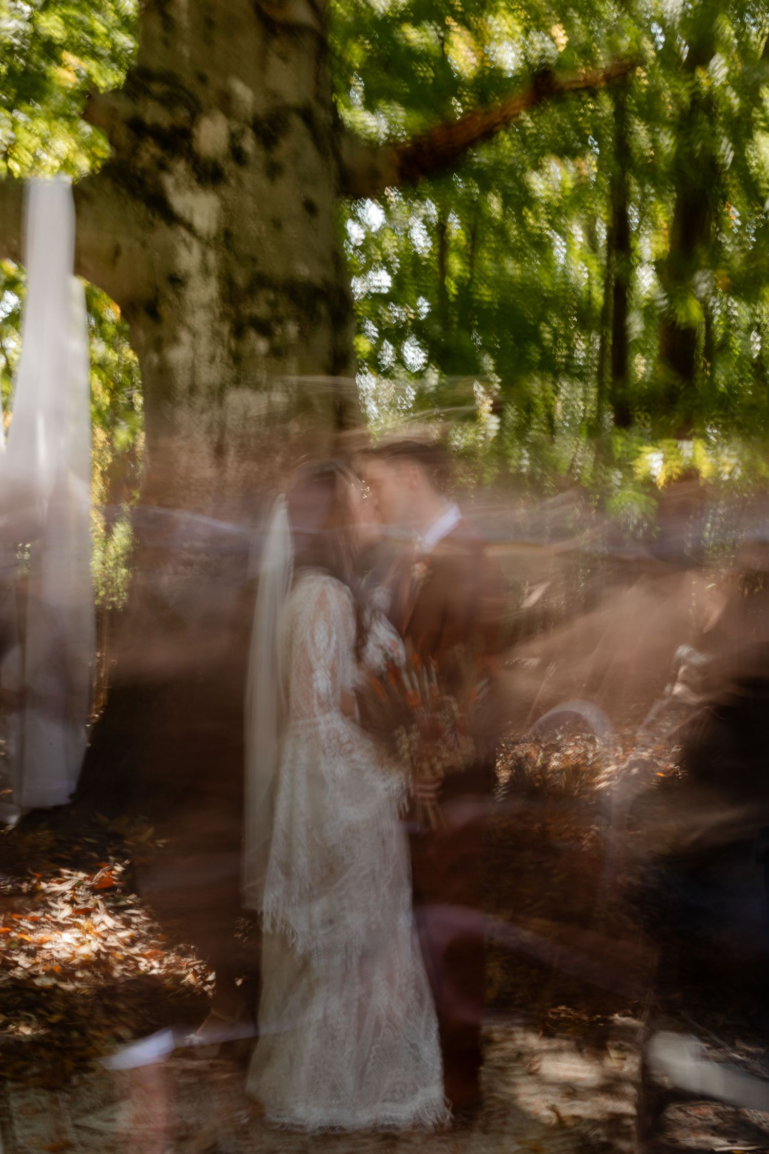 Artistic long exposure shot creating ghost-like figures under tree canopy.