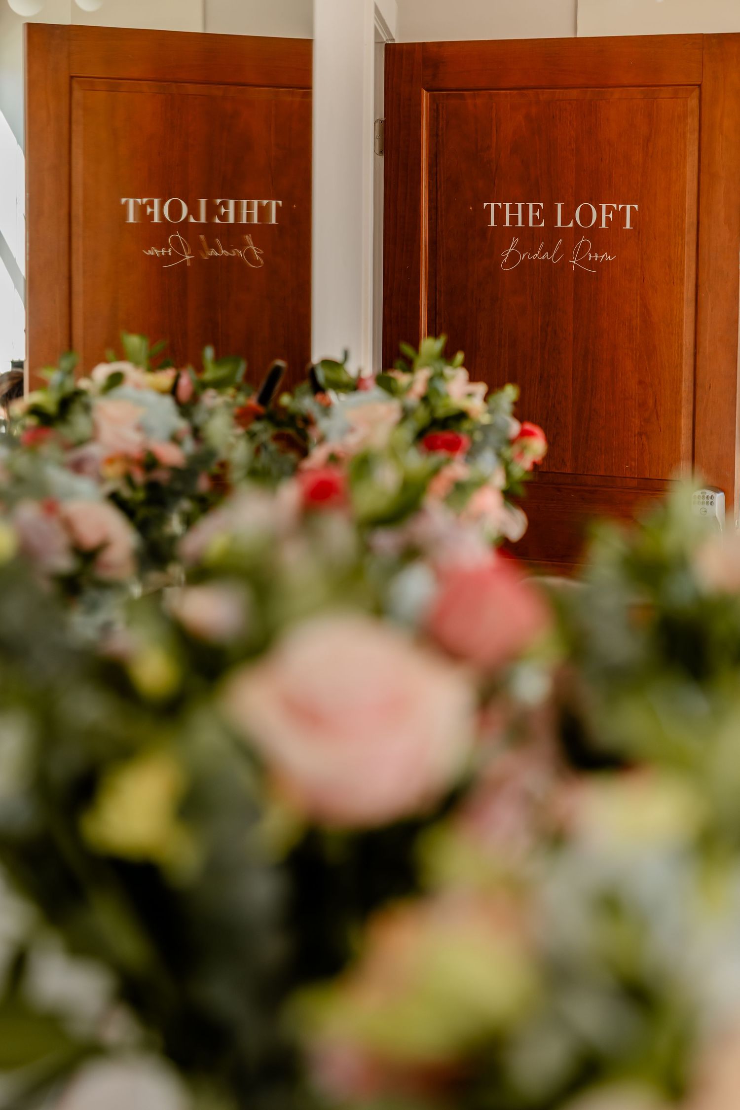 Wedding venue sign on wooden door with soft focus floral arrangements in foreground.