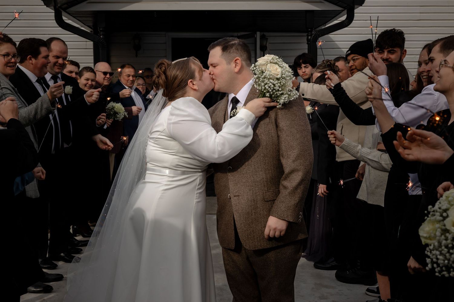 Wedding ceremony crowd surrounds couple sharing their first kiss as newlyweds.