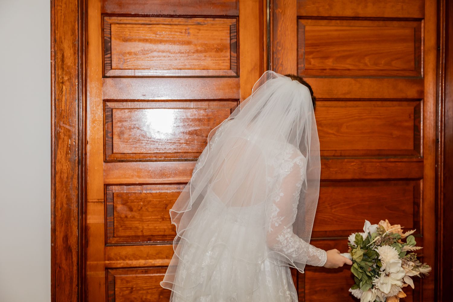 Wedding details featuring white veil against natural wood paneled doors.