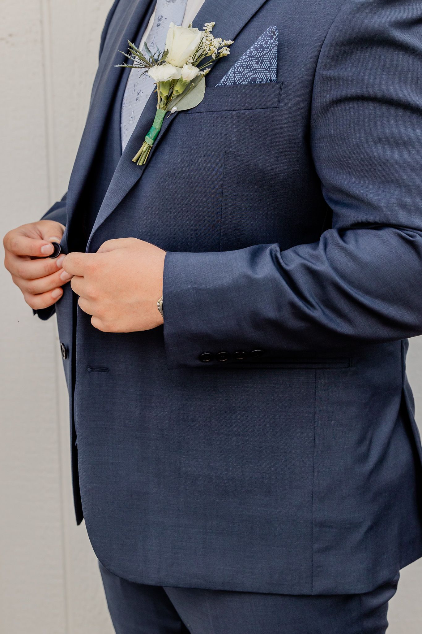 Close-up detail of navy blue suit jacket with white boutonniere flower pinned to lapel.