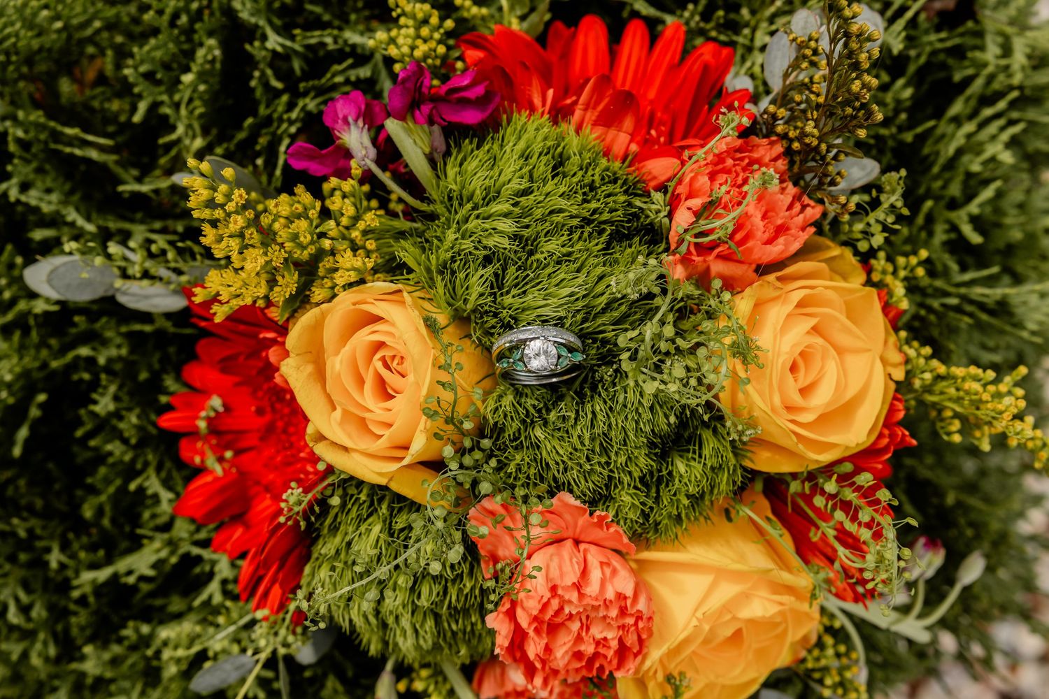Vibrant wedding bouquet featuring red, orange, and yellow roses with mixed greenery.