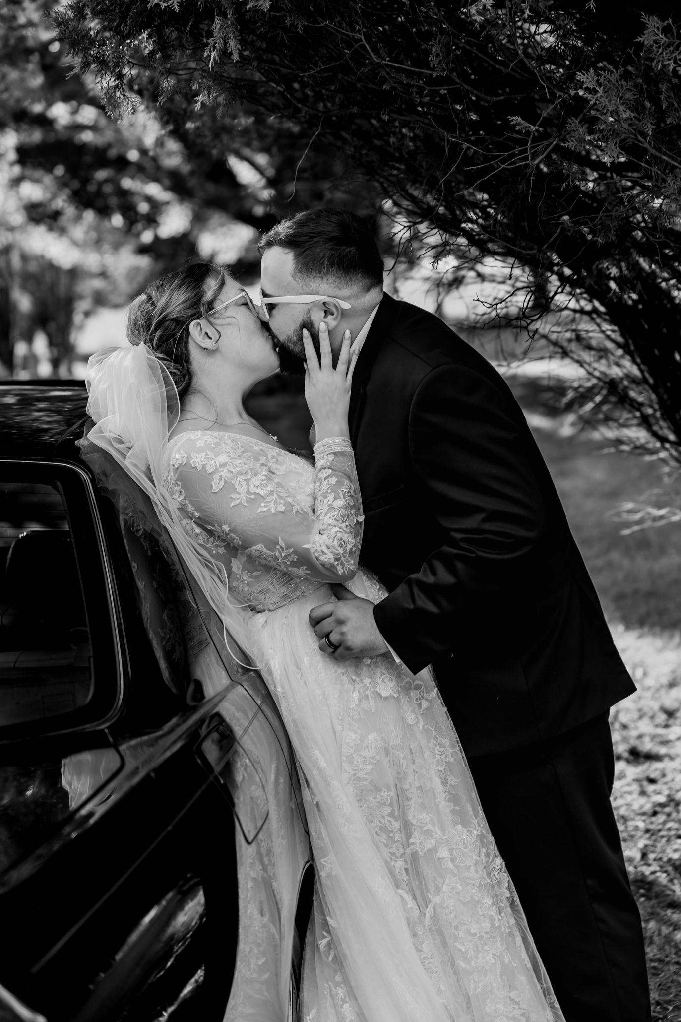 A romantic black and white wedding photoshoot sequence showing a couple sharing a kiss near a car.