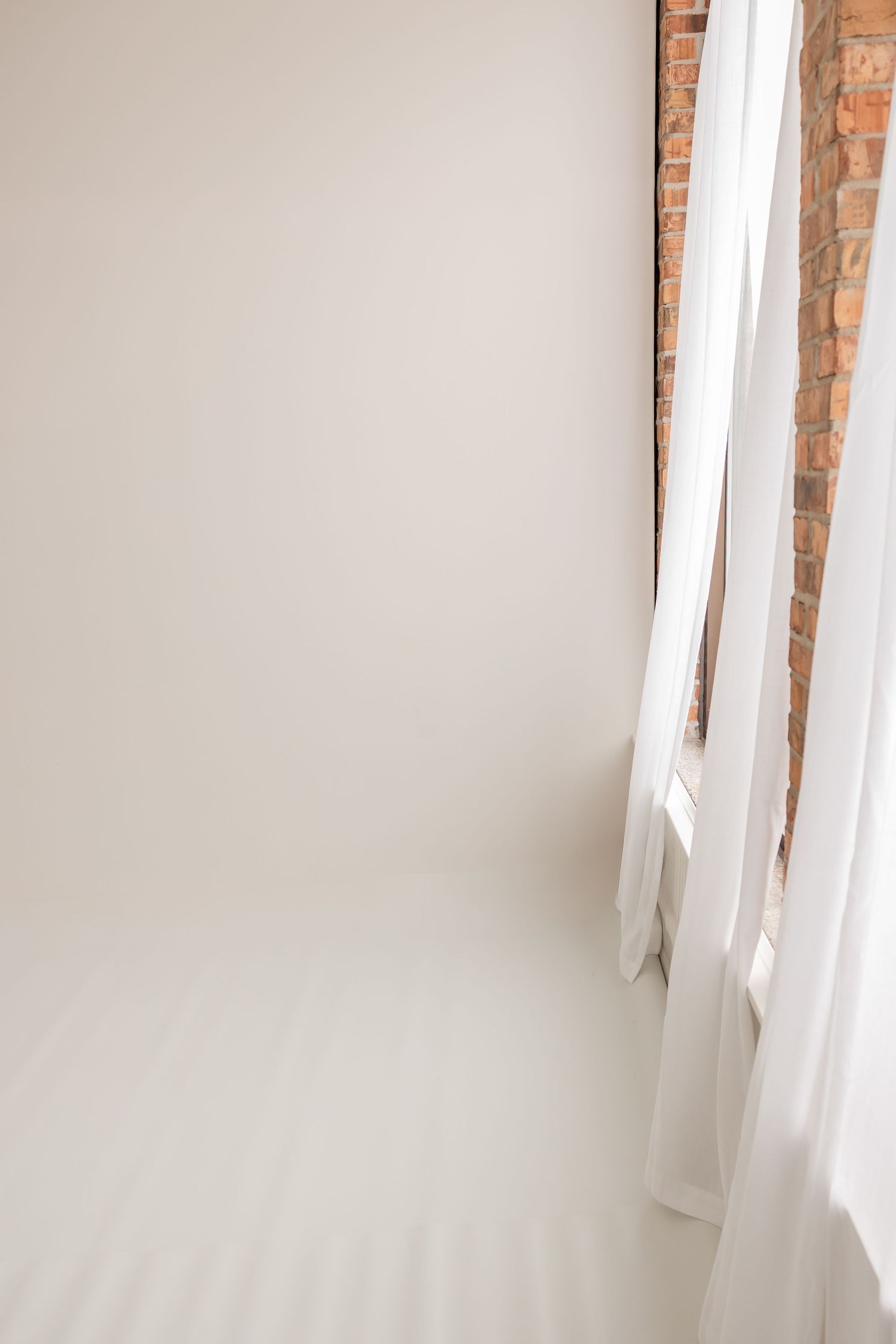 White curtains hanging in front of brick walls create a bright, minimalist interior space with natural lighting.