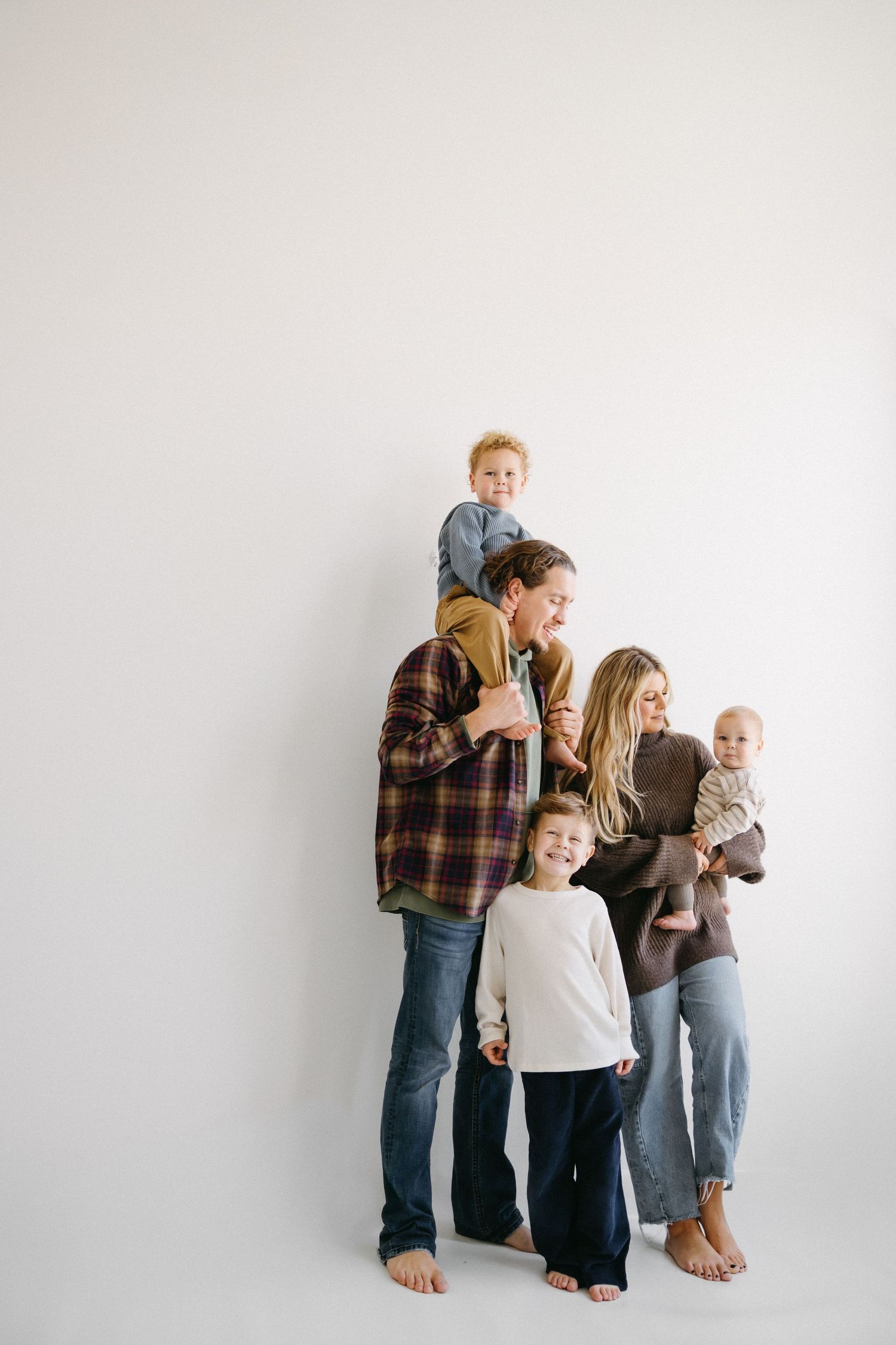 A sequence of four minimalist studio photos showing a family group arranged in different poses against a white background.