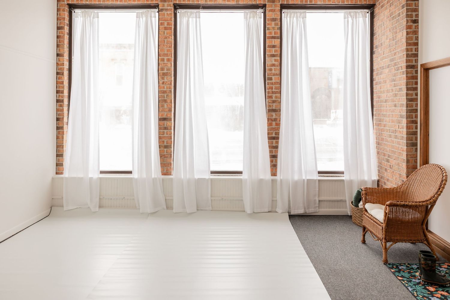 Modern loft apartment interior with exposed brick walls, white curtains, and large windows letting in natural light.