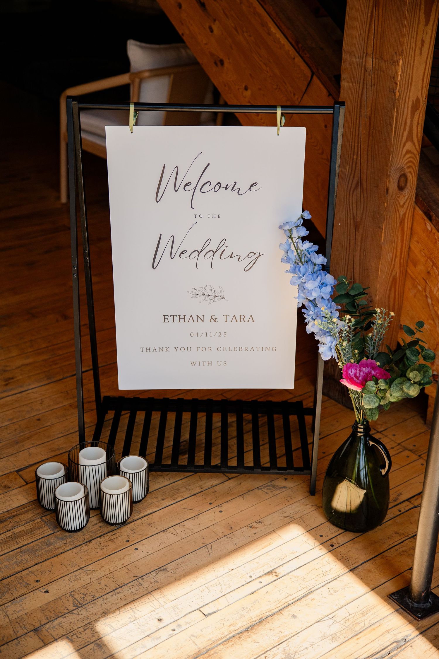 Wedding welcome sign with blue flowers displayed on wooden floor with votive candles.