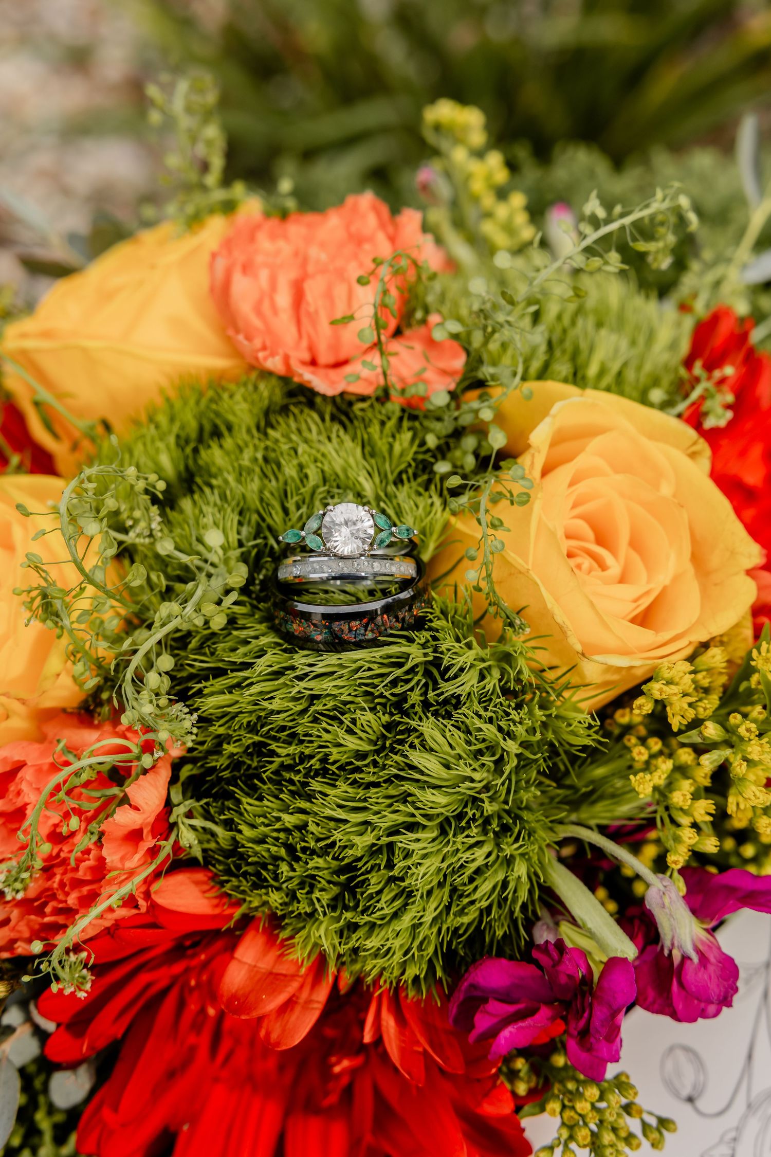Vibrant wedding bouquet featuring yellow roses, red flowers and lush greenery with ring detail.