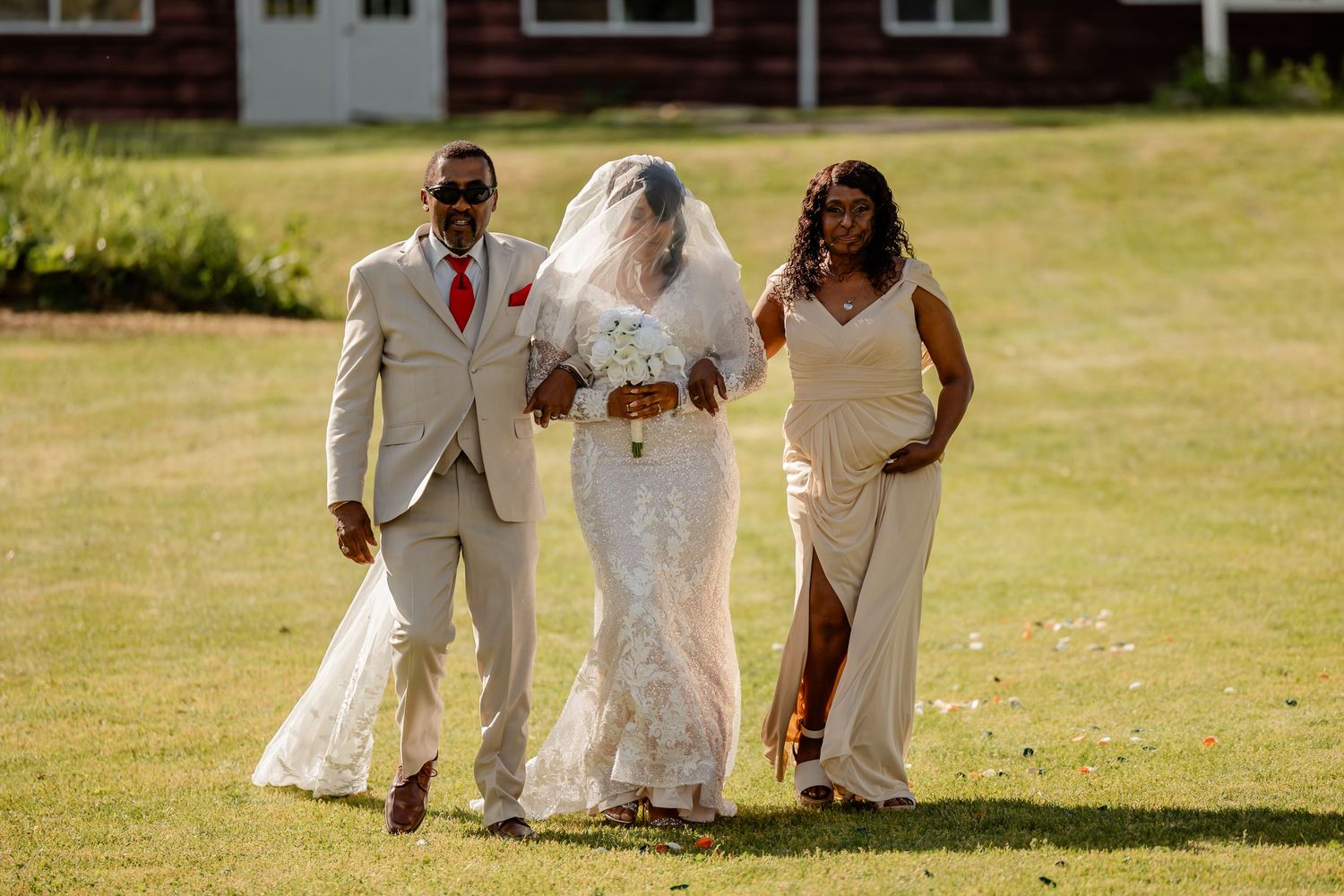 Wedding party walks together on grassy lawn during outdoor celebration.