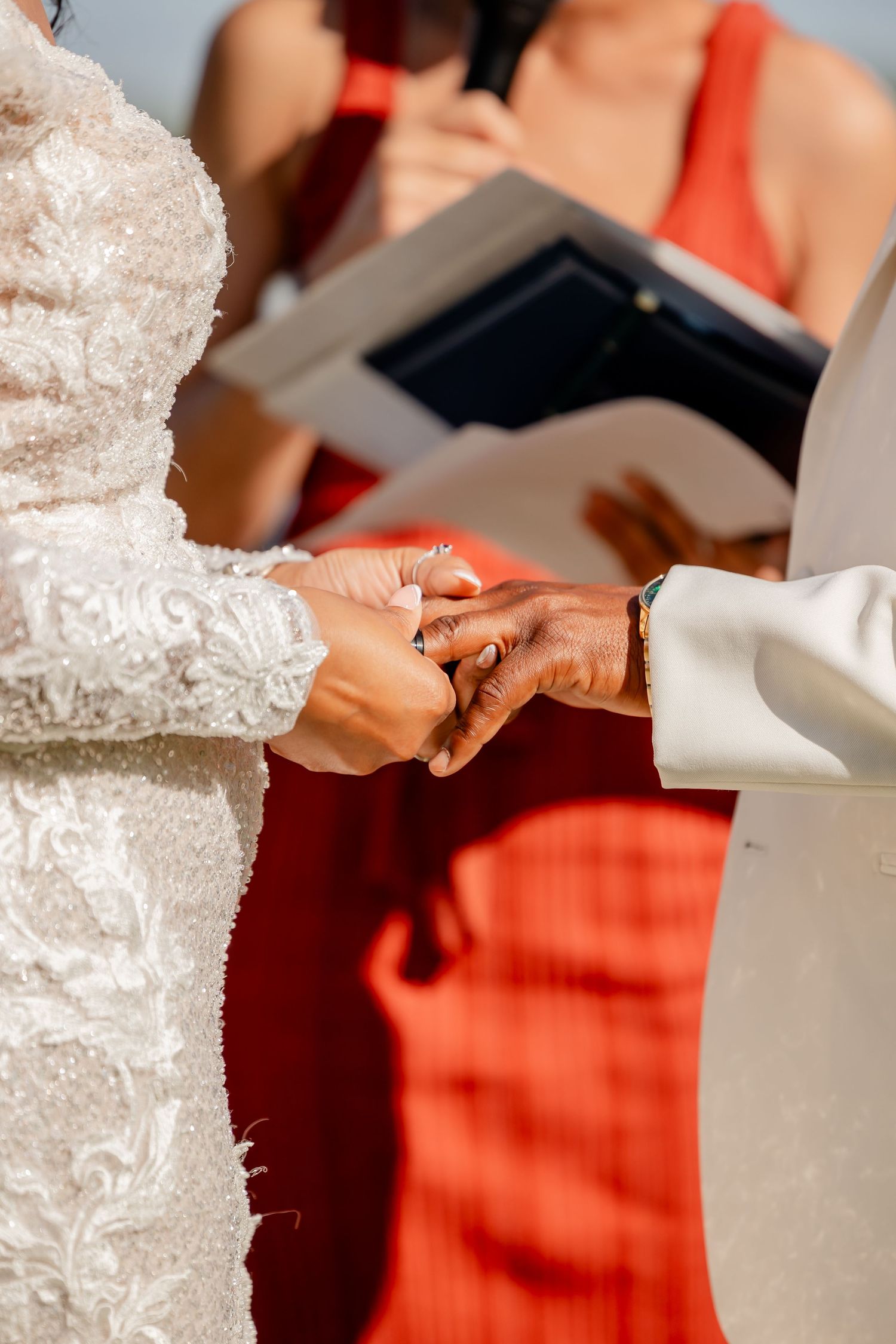 Close up of hands exchanging rings during wedding ceremony with lace dress detail.