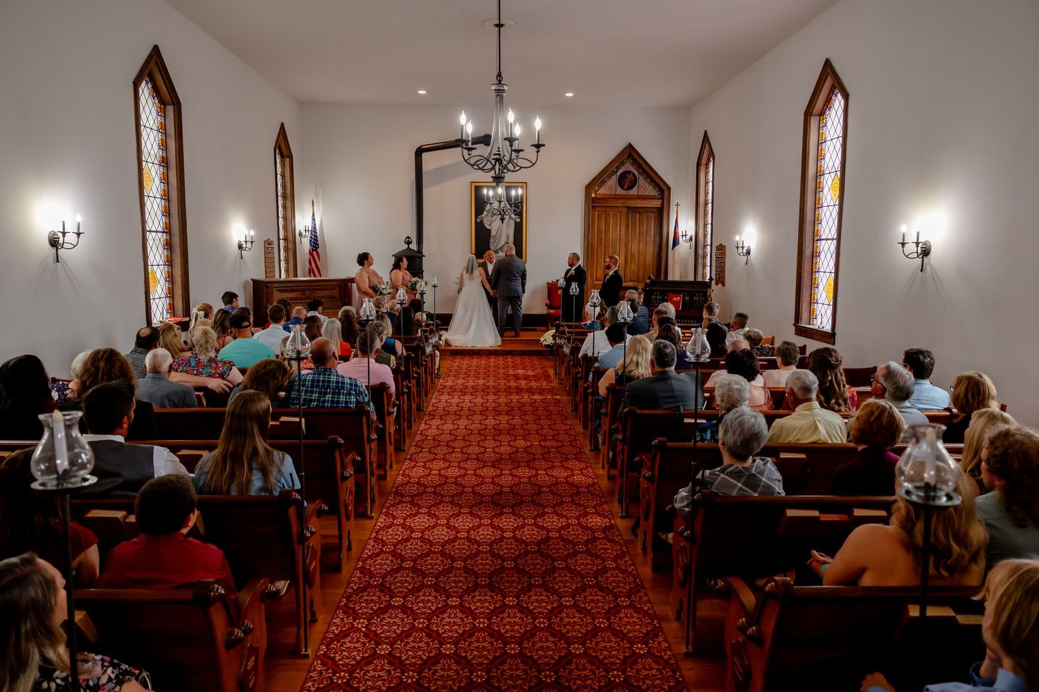 Interior view of a church sanctuary with wooden pews and red carpeting during a gathering or service.