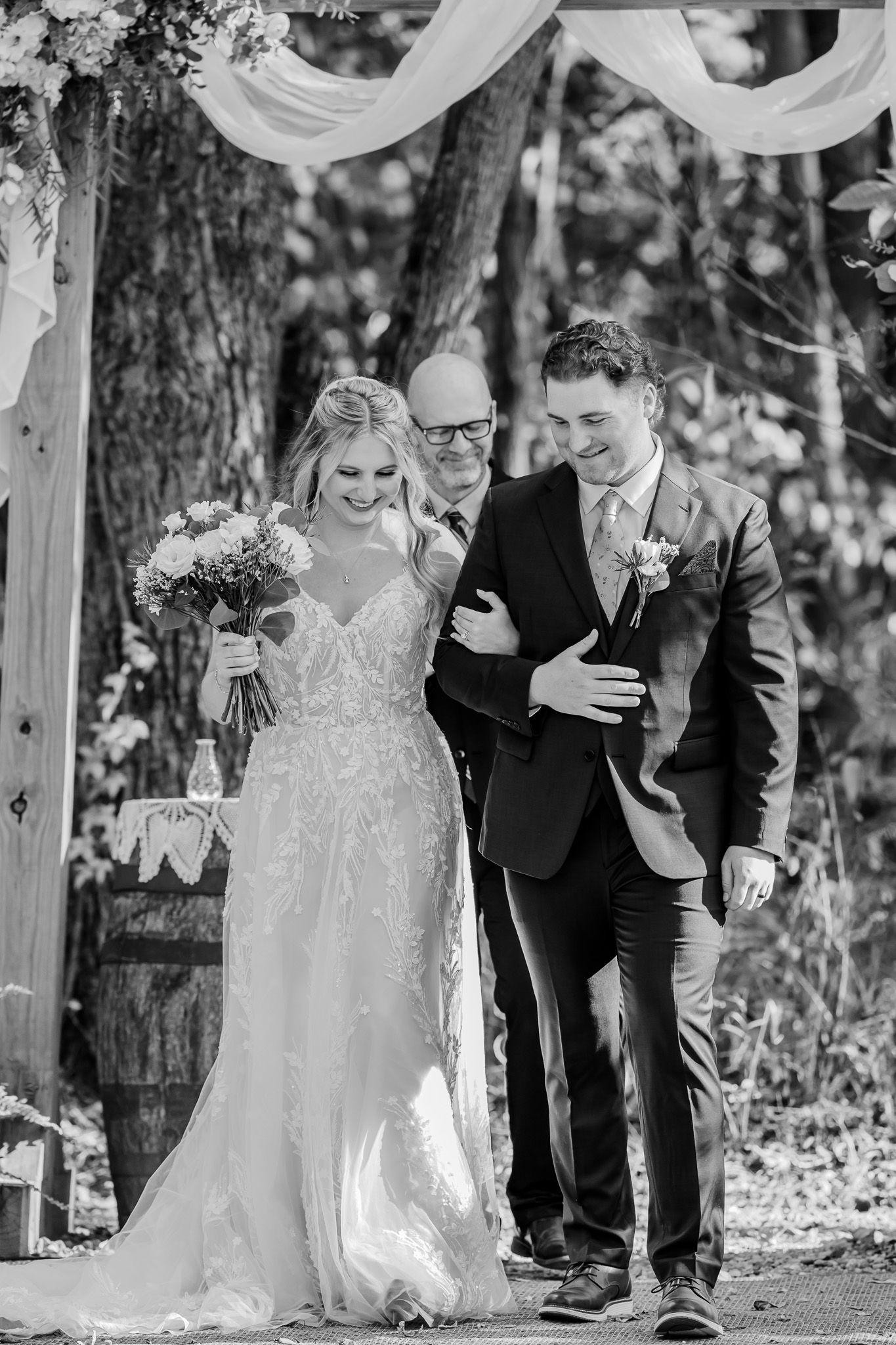 Black and white wedding ceremony photos showing couple walking together under draped fabric decorations outdoors.