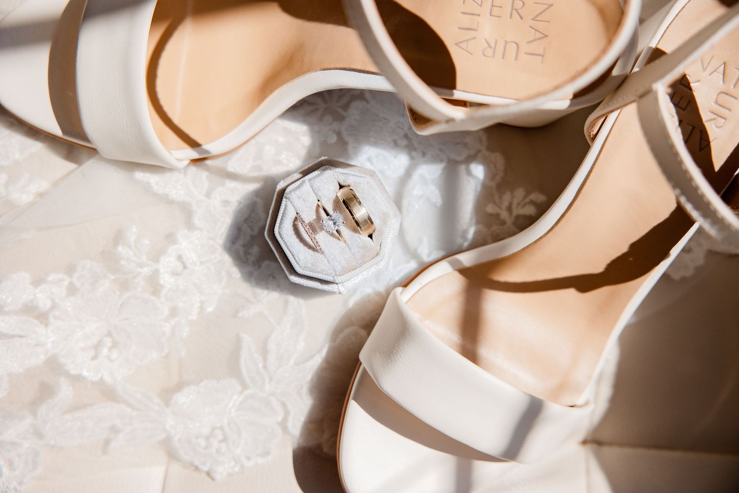 Close-up details of wedding rings and jewelry on textured white surface.