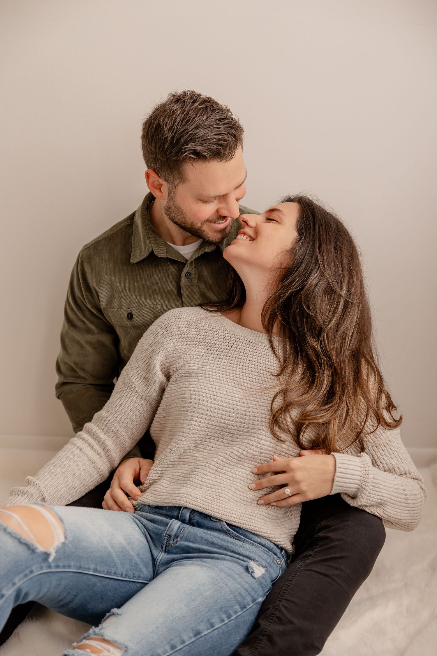 A couple in casual sweaters and jeans share intimate moments while relaxing together on a light colored couch.
