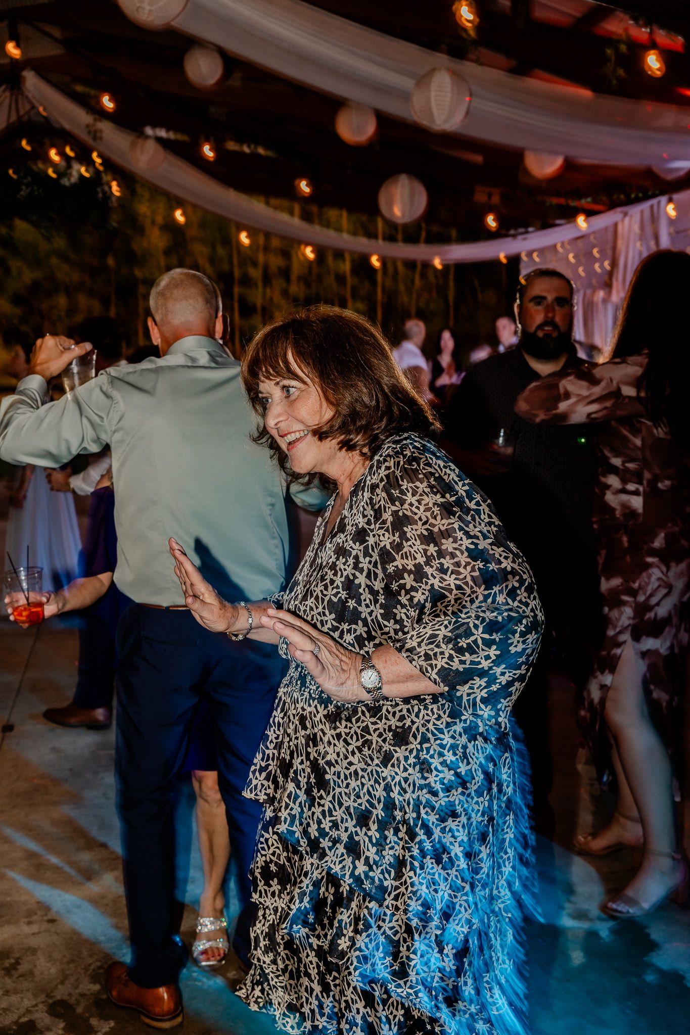 Couples dancing together at a dimly lit reception with blue lighting and paper lantern decorations overhead.