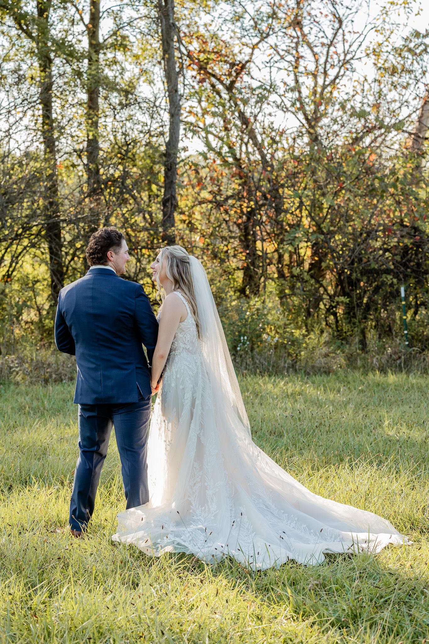 A bride and groom share a romantic moment in a sunlit meadow with trees in the background.