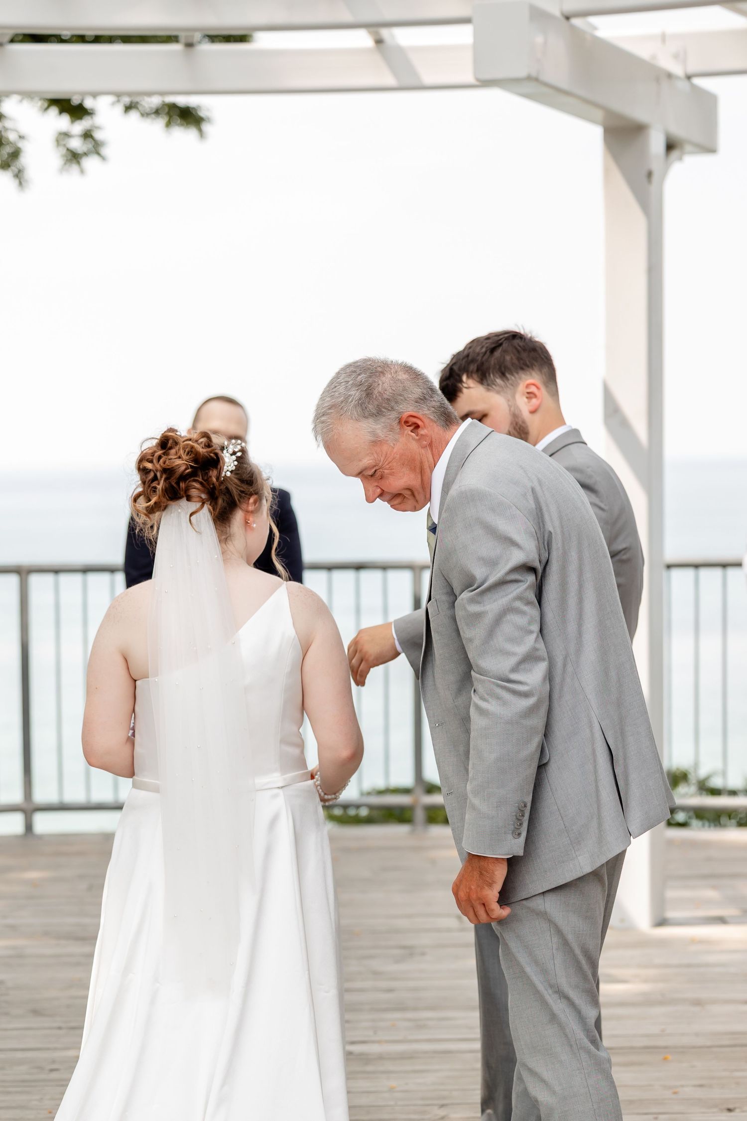 Emotional wedding ceremony moments captured on a waterfront deck with grey and white attire.