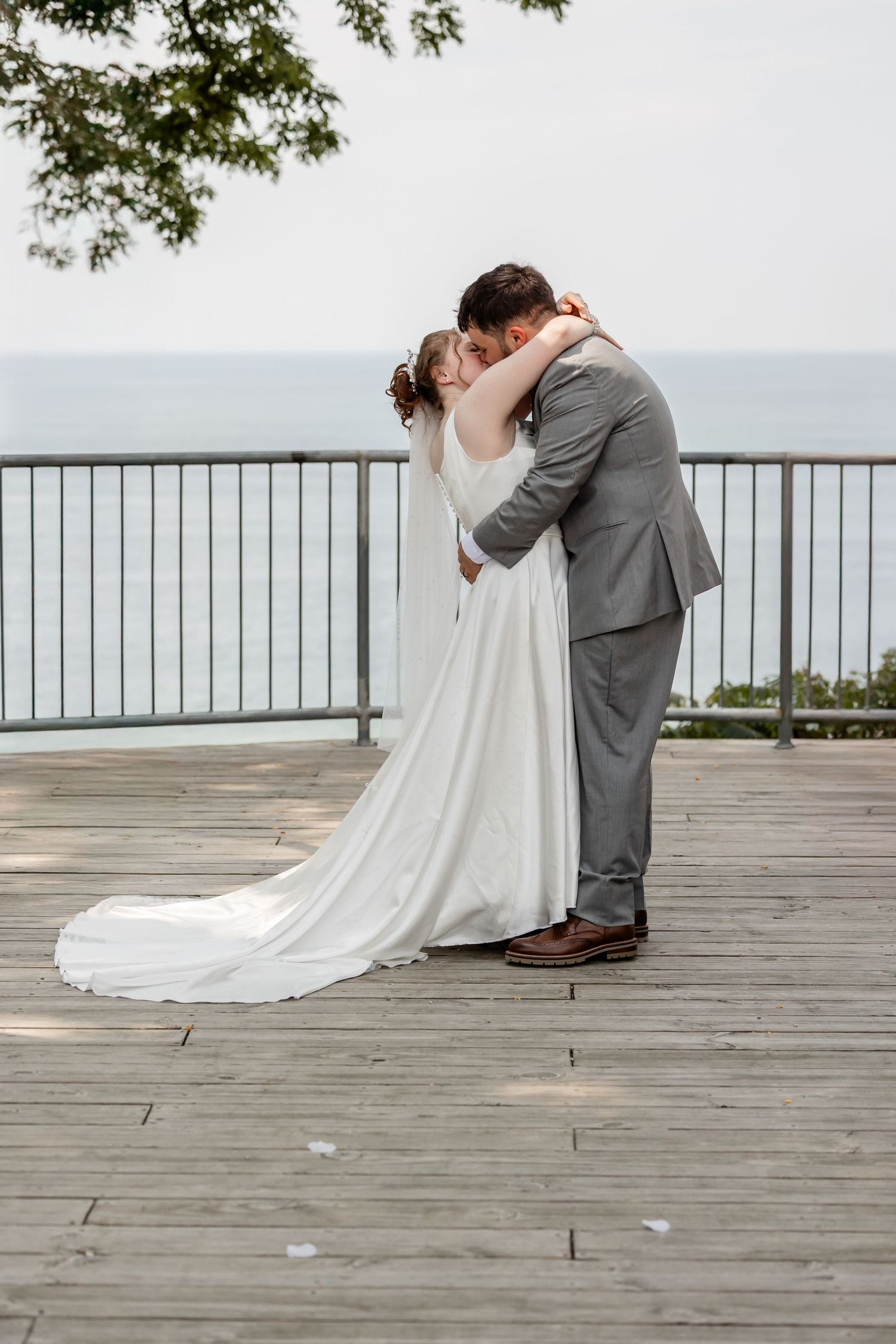 Romantic moment captured on wooden deck overlooking water with flowing white wedding dress.