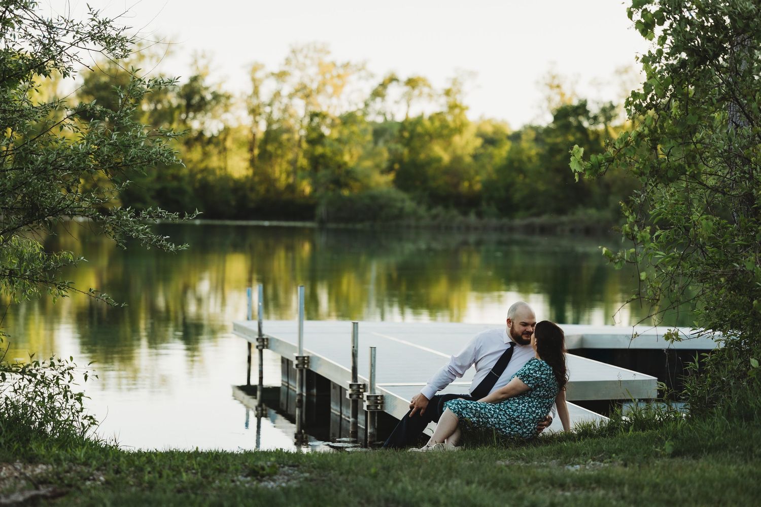 A couple shares an intimate moment on a dock overlooking a serene lake at sunset. Dowagiac