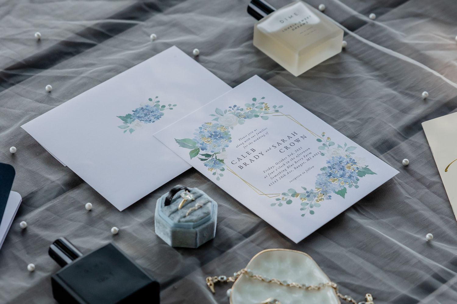 Wedding invitation with delicate blue and purple floral designs displayed alongside a small gift box and accessories.