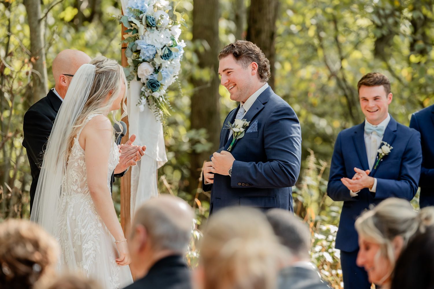 Couple exchanging vows during an intimate forest wedding ceremony with guests looking on.
