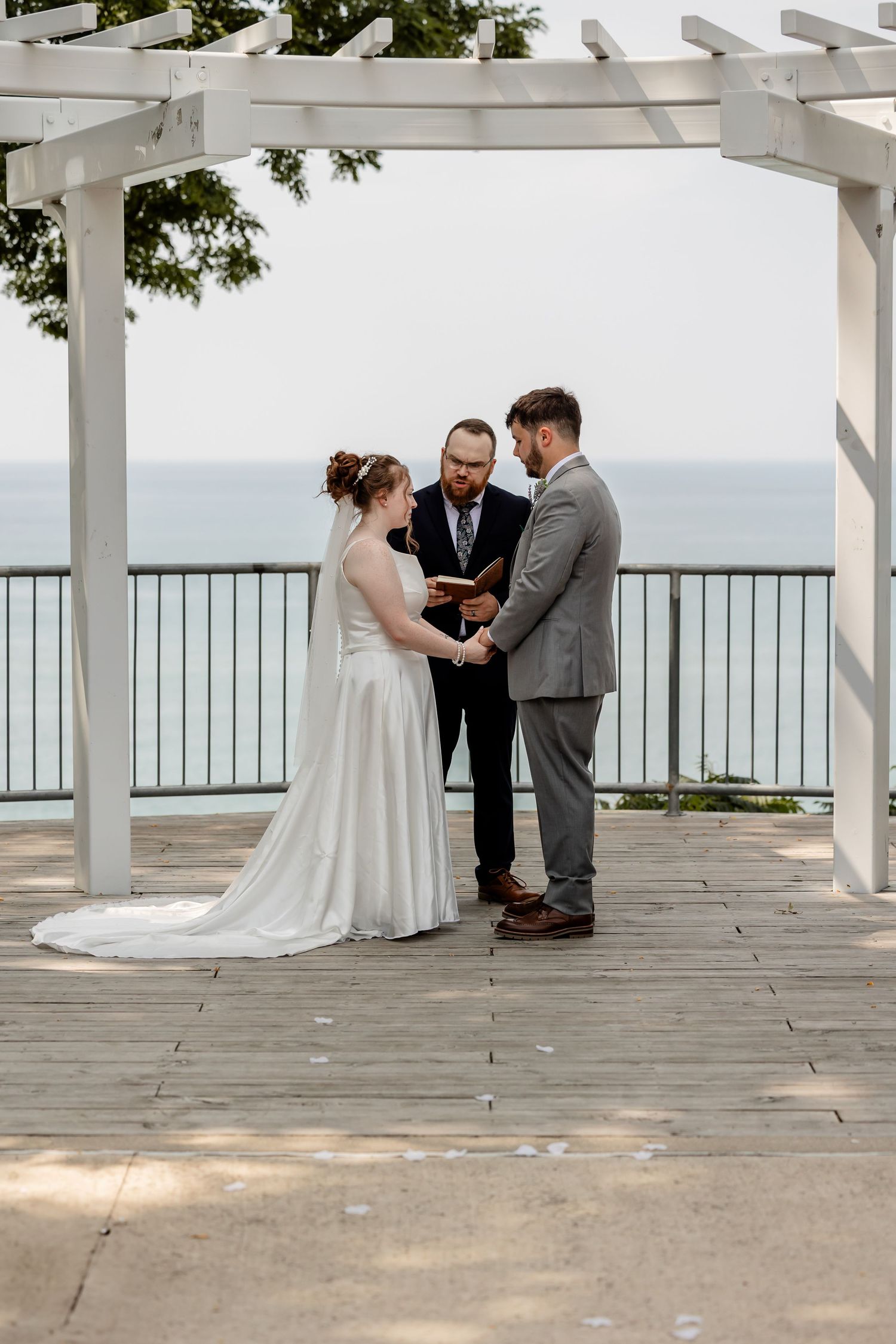 Waterfront wedding ceremony under white pergola with ocean view in the background.