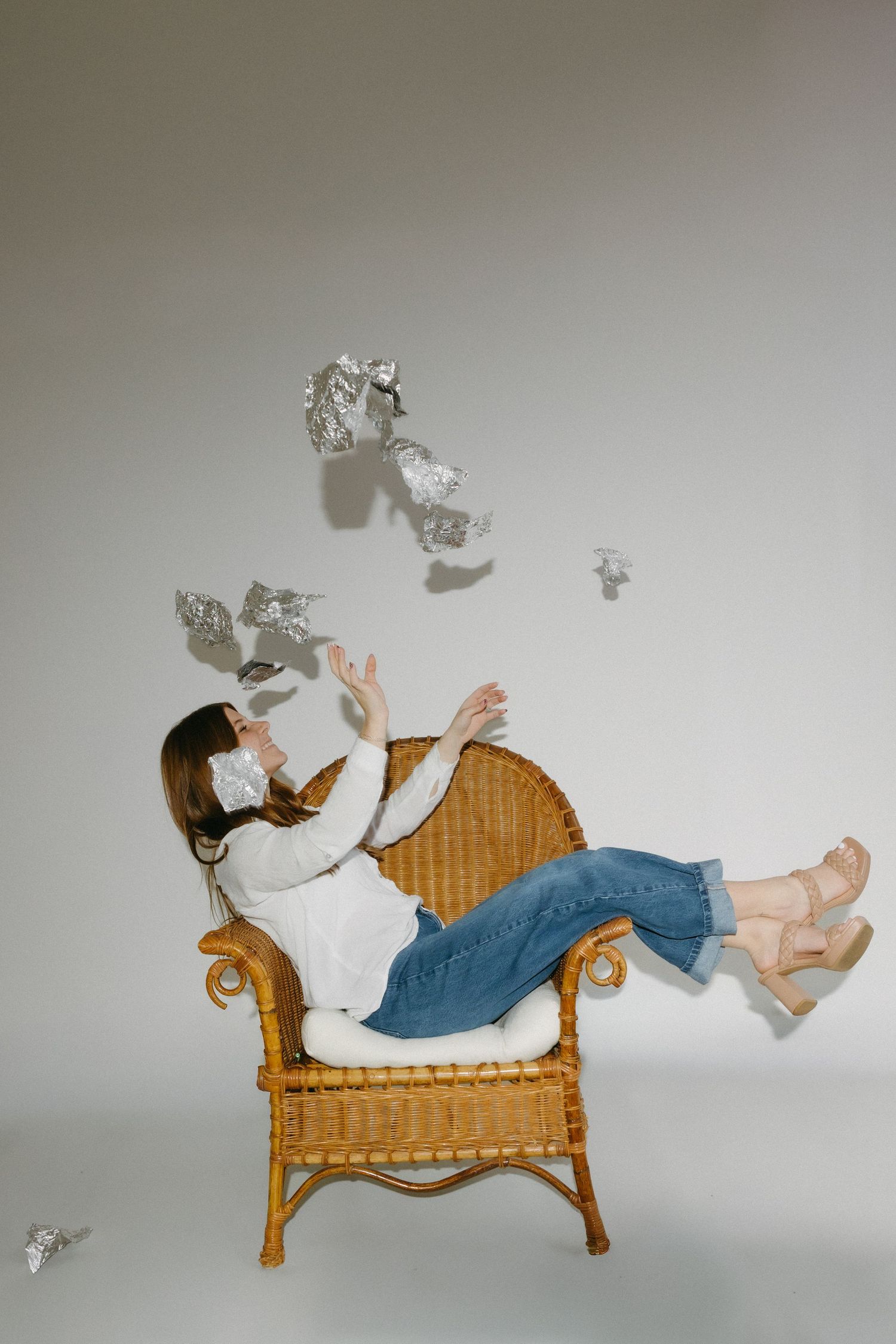 A person in jeans reclines on a wicker chaise lounge while papers float and scatter in the air around them.