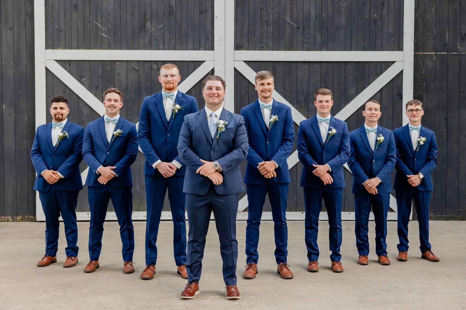 Groomsmen in matching navy suits and brown shoes sit lined up showing their colorful socks in a fun wedding photo.