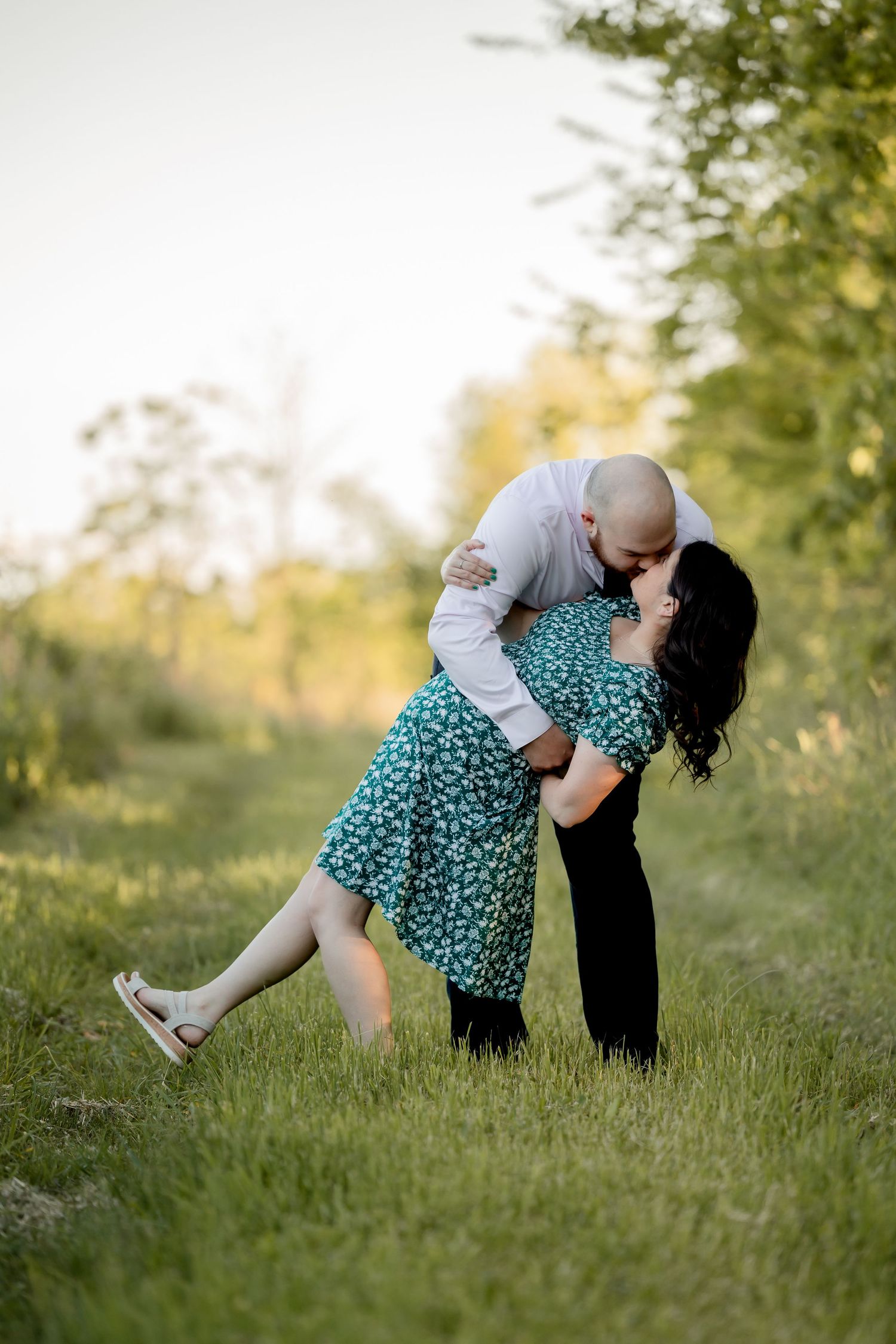 Playful couple performs a romantic dip pose in green grass during sunset.