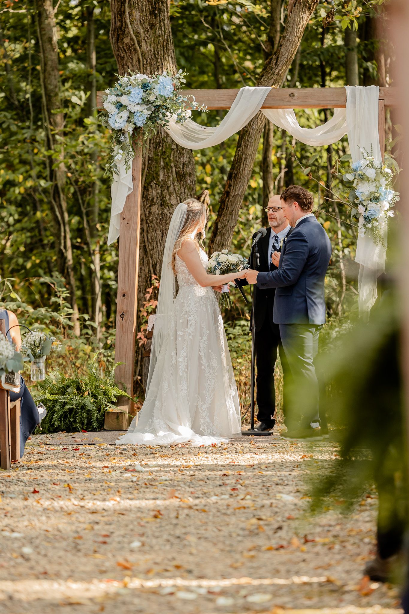 A romantic first look moment between a couple on a tree-lined path covered in autumn leaves.