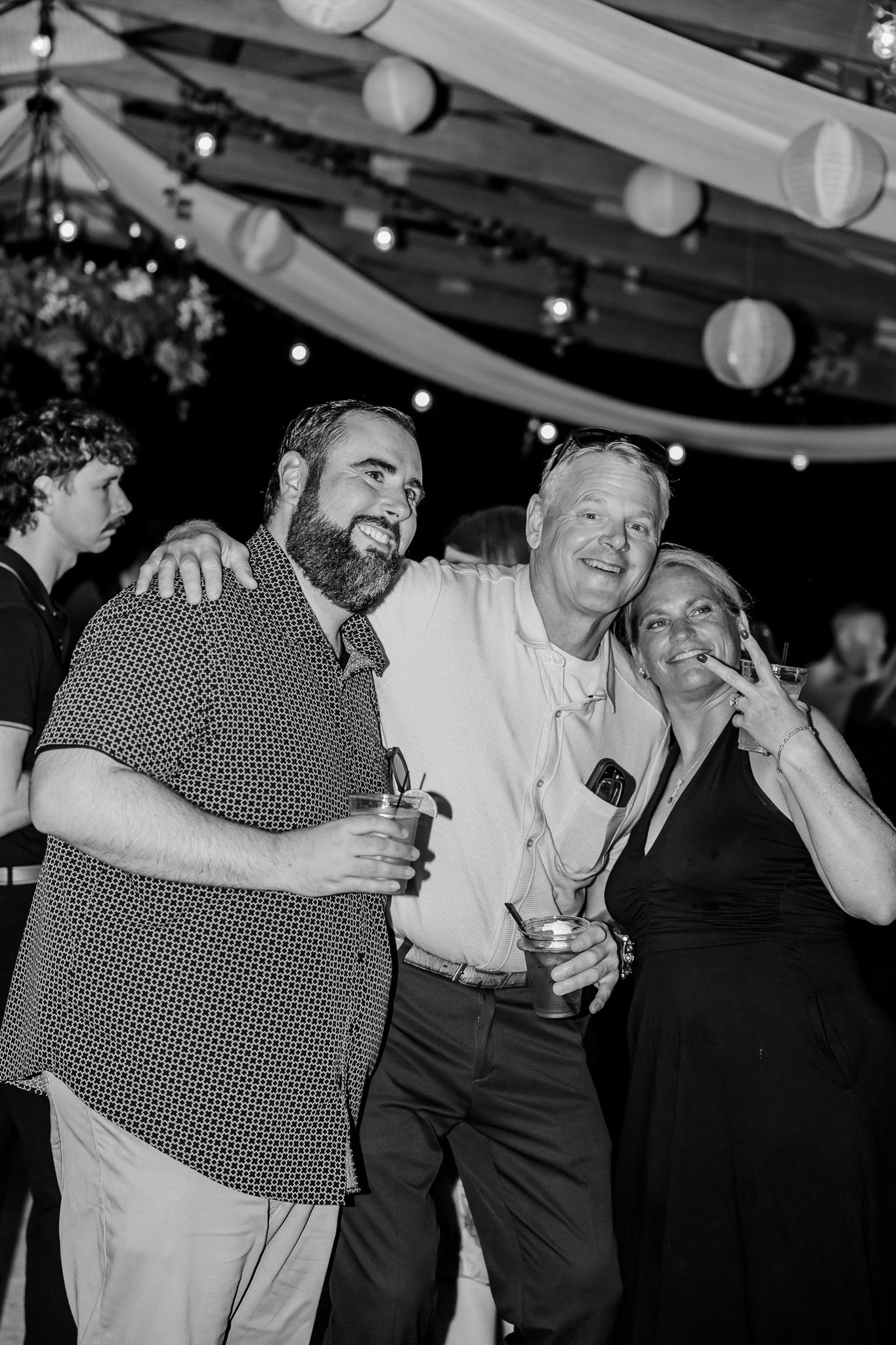 A group of people dancing and celebrating at a wedding reception under string lights and paper lanterns.