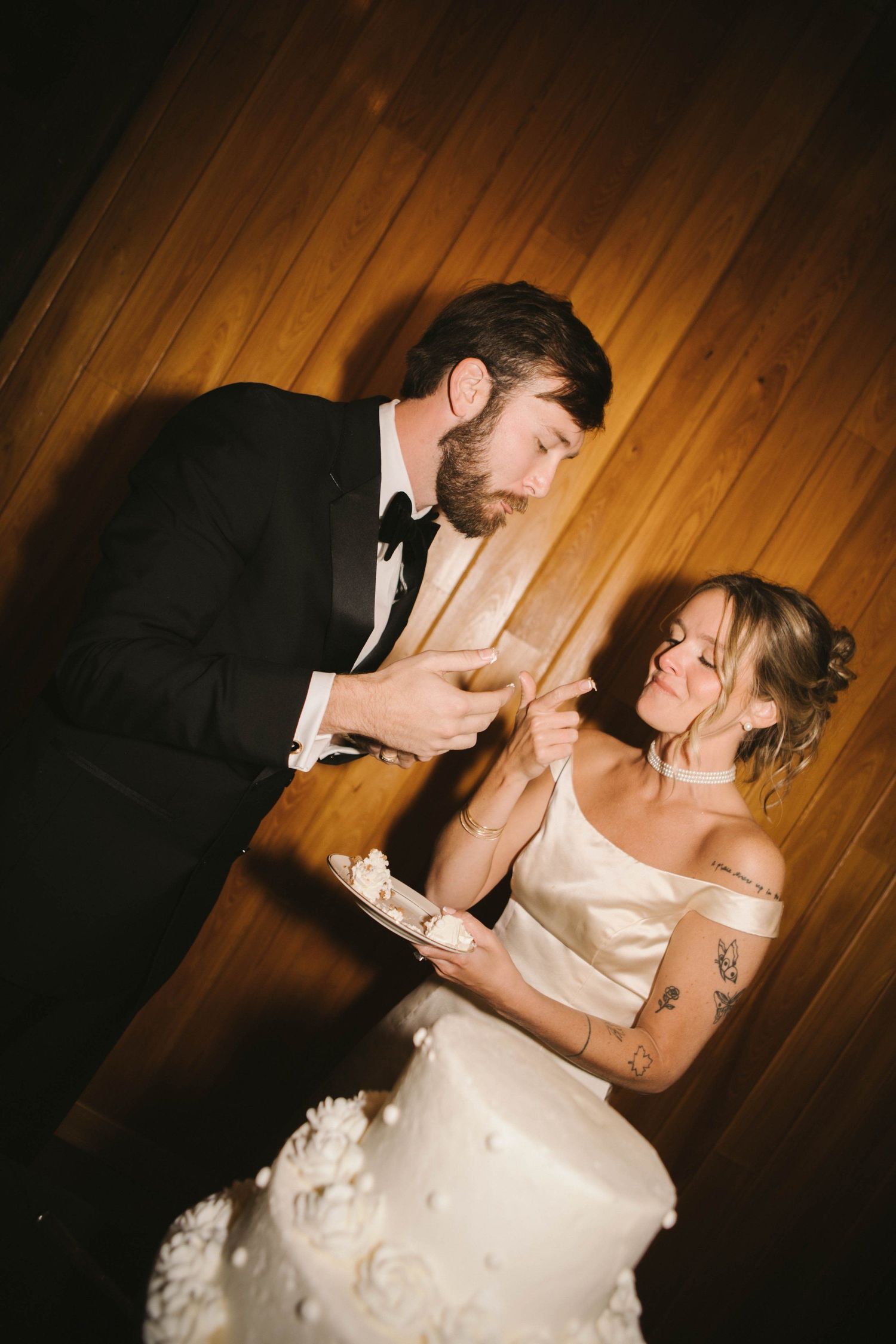 Couple sharing cake at their wedding reception in a rustic wooden venue.